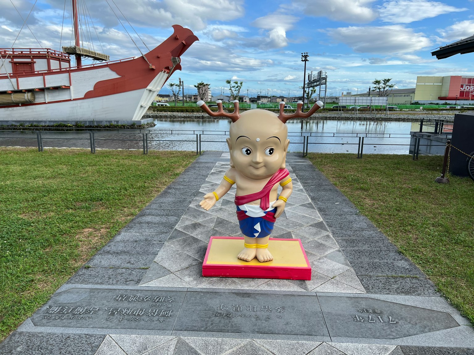 Una estatua de un personaje de dibujos animados en un parque con un barco al fondo