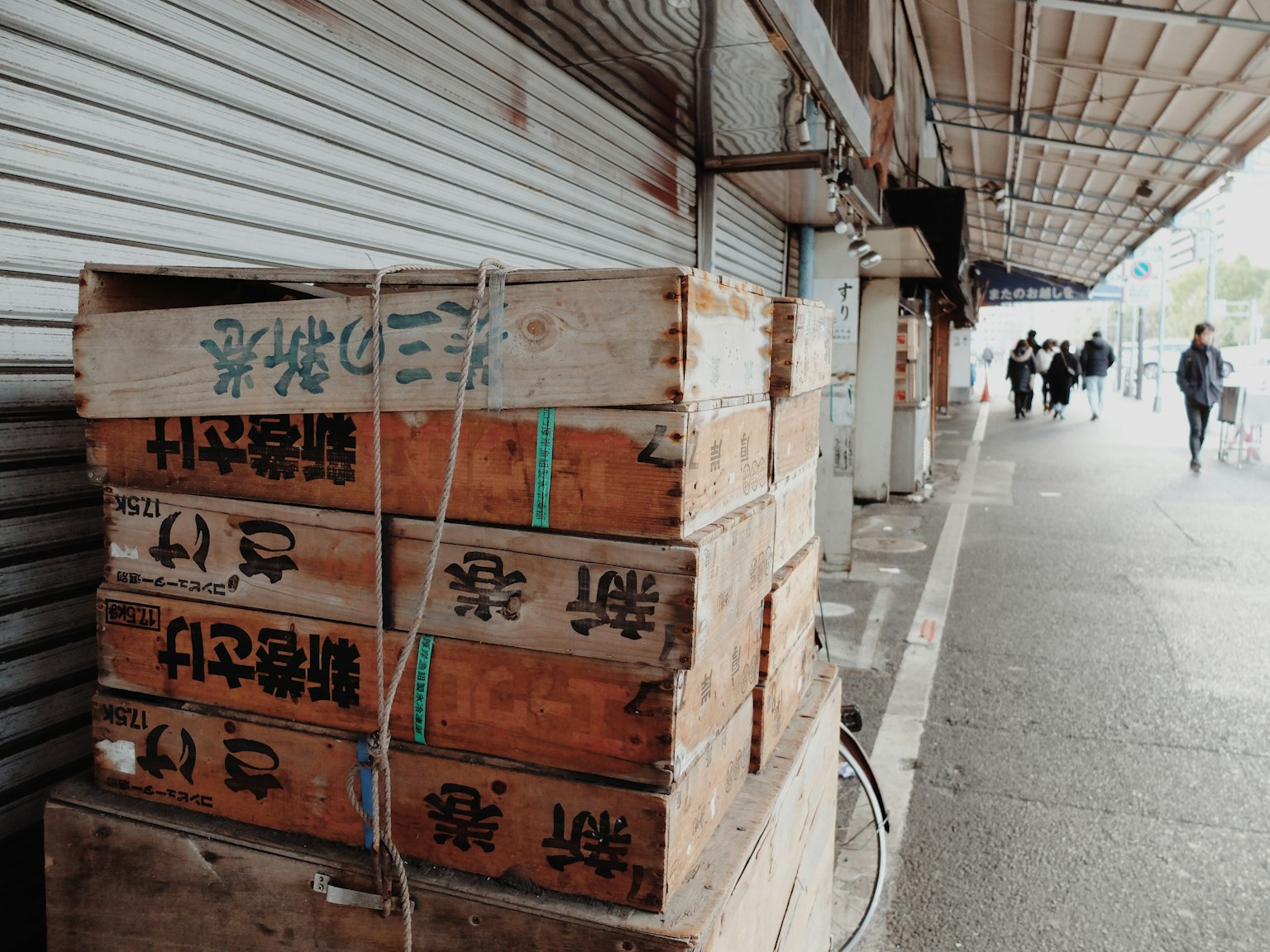 Stacked wooden crates on a sidewalk with people walking in the background