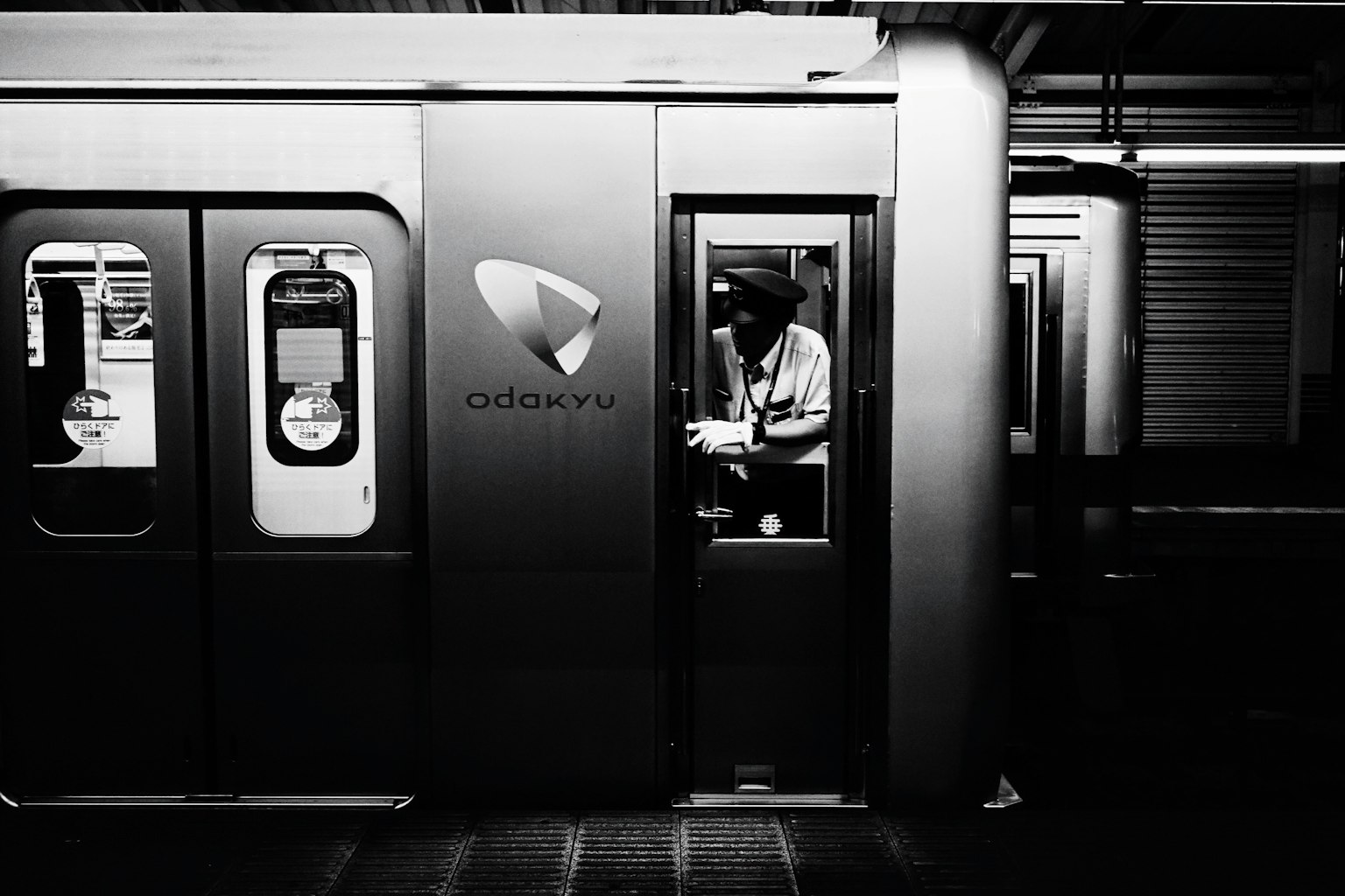 Black and white image of an open subway train door with a driver operating inside