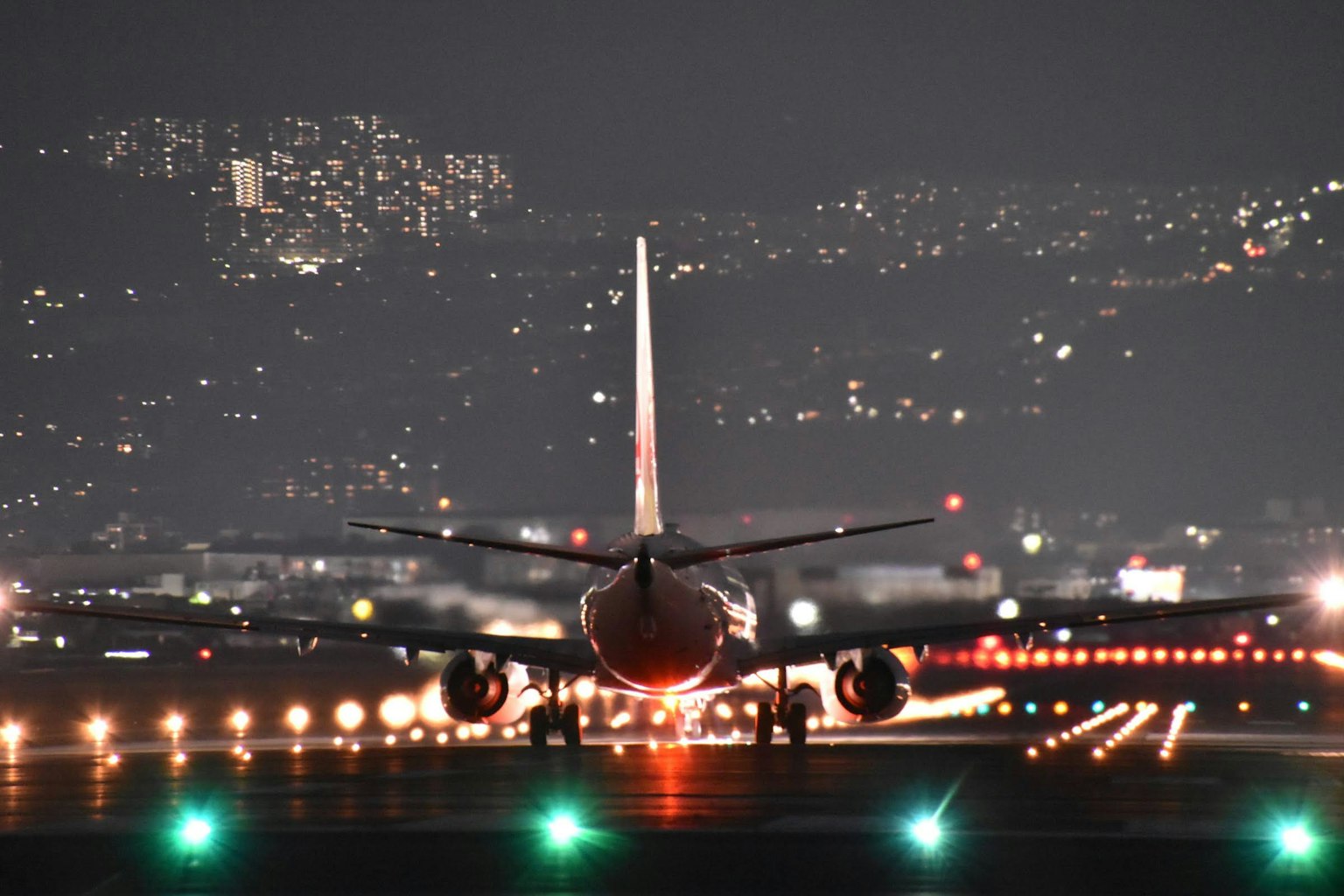 Avion rouge sur la piste de nuit avec des lumières de la ville en arrière-plan