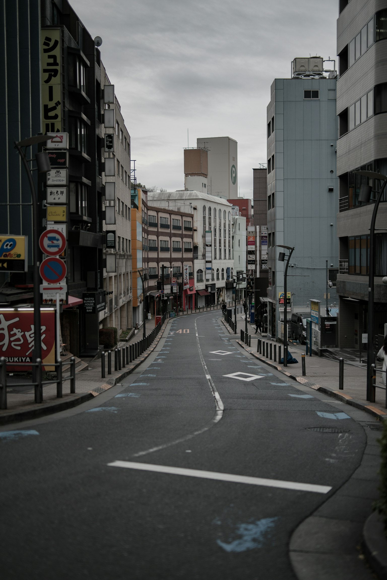 Calle urbana tranquila con pocos peatones, cielo gris, flanqueada por edificios