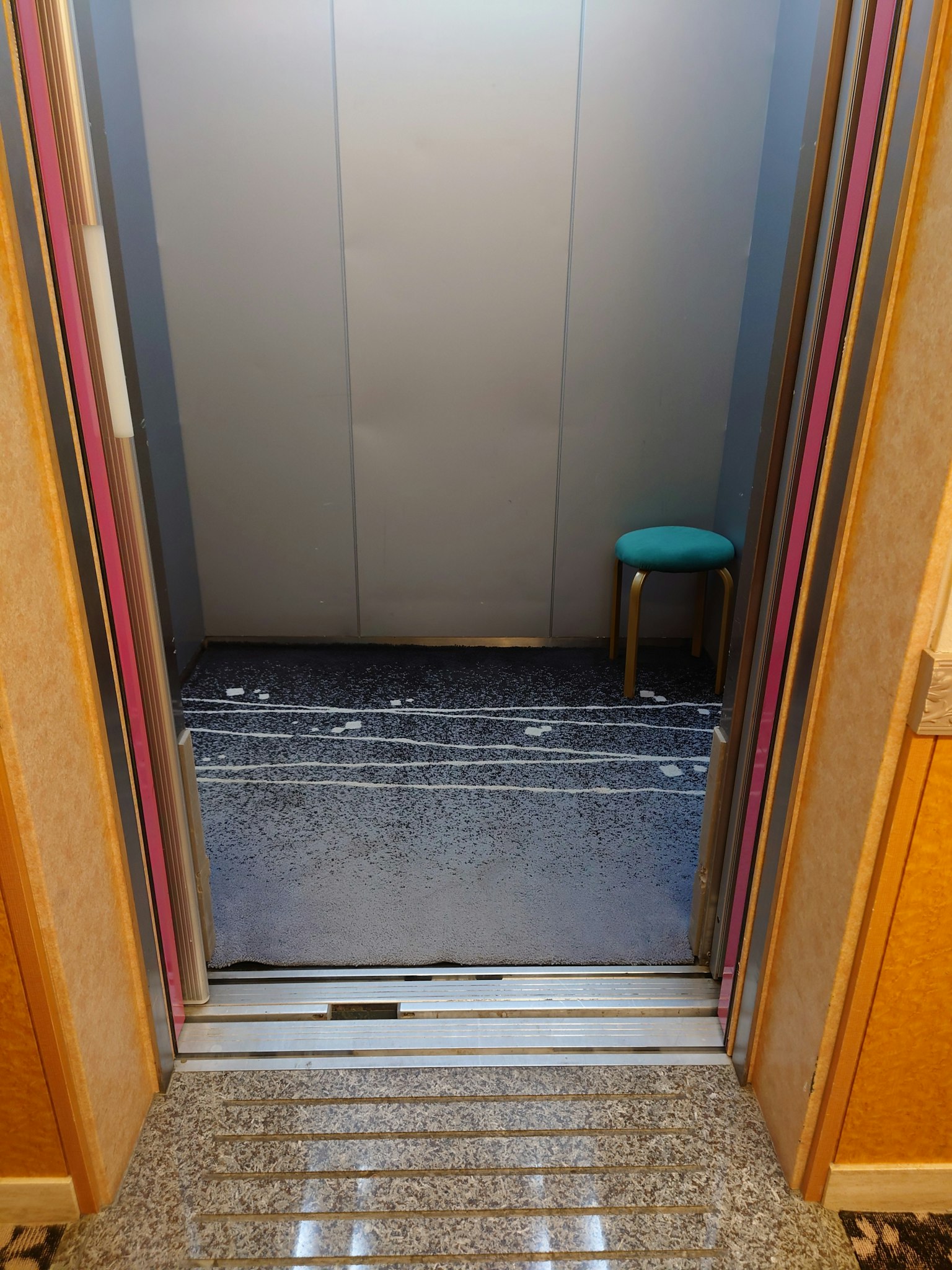 Entrada del ascensor con una silla azul y suelo de baldosas