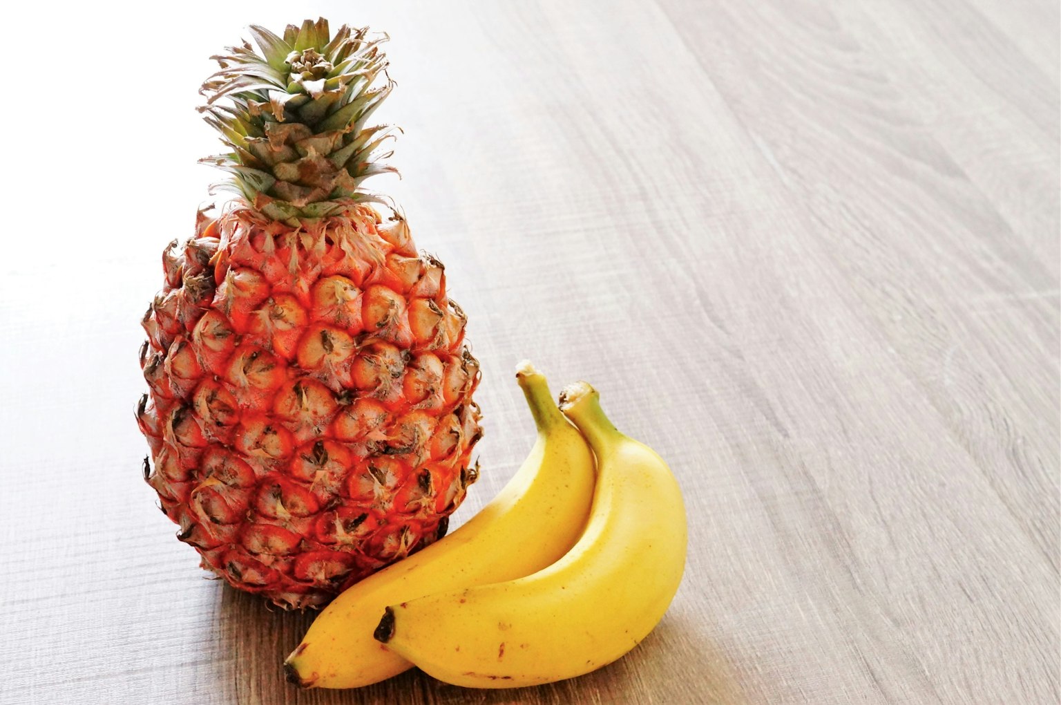 Una piña y plátanos colocados sobre una mesa de madera