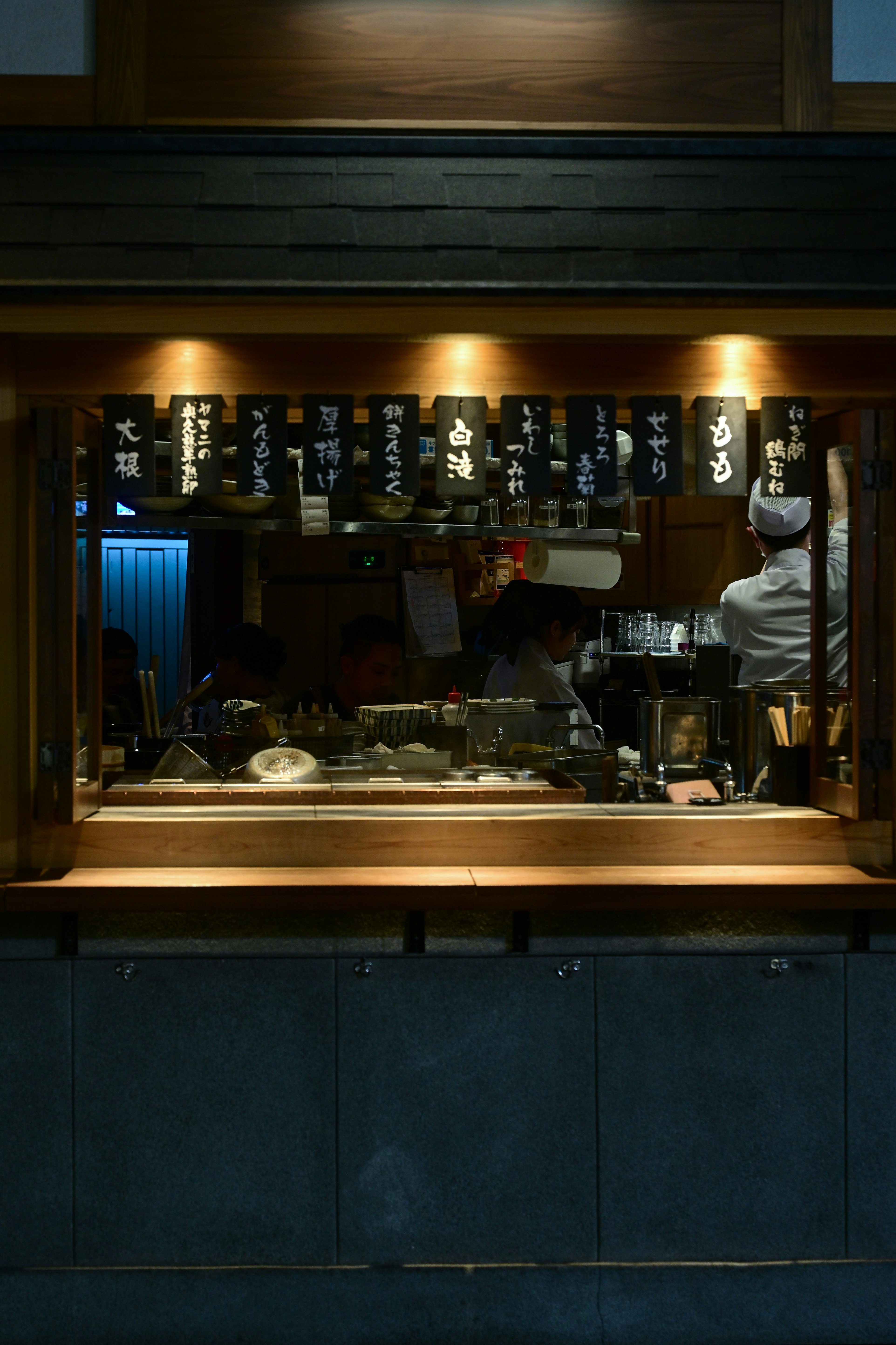 木製カウンター越しの小さな飲食店の厨房とメニューの暖色照明