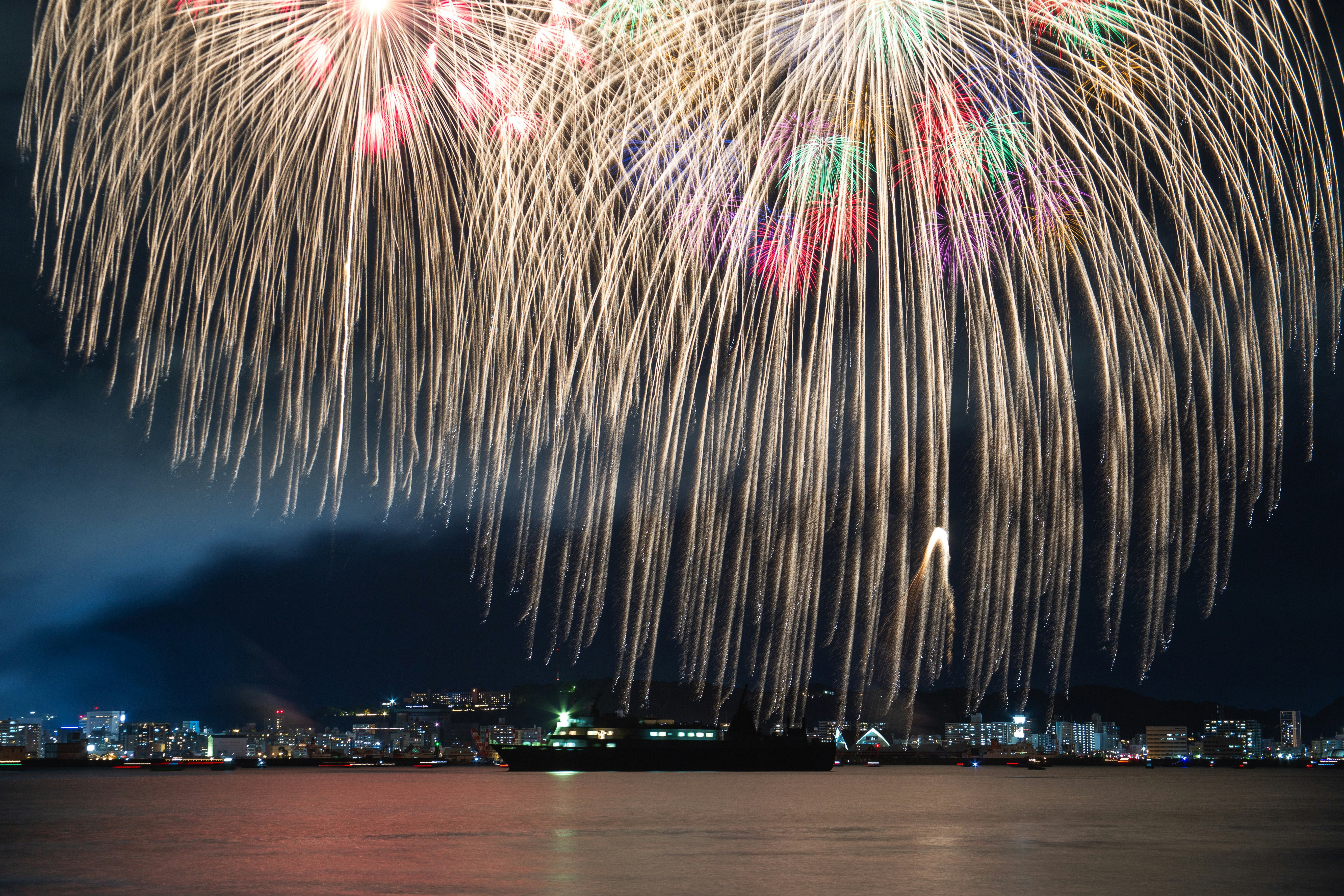 夜空に咲く花火と川沿いの街並み
