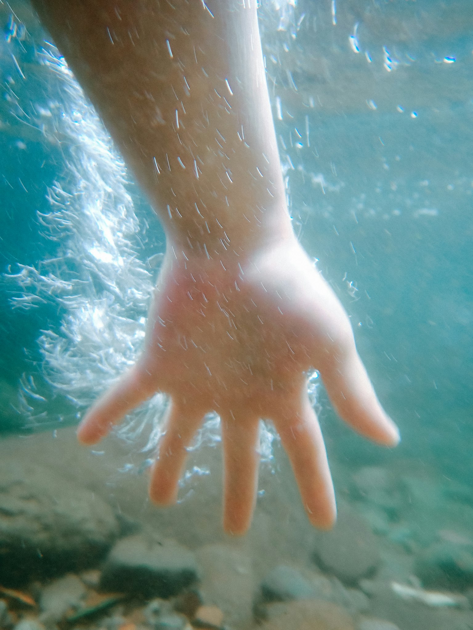 Eine Hand, die unter Wasser greift, umgeben von Blasen