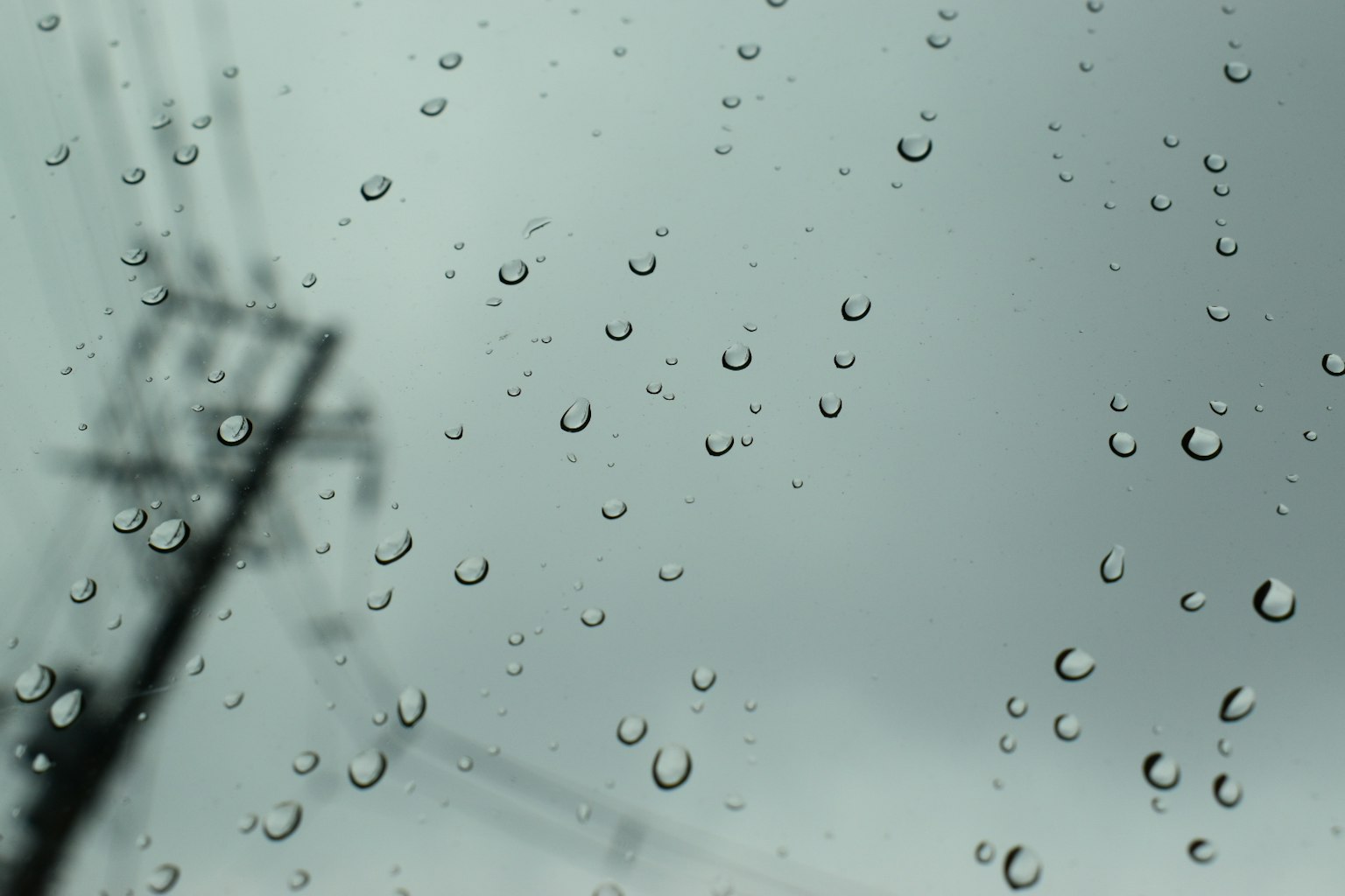 Raindrops on a window with a gray sky and silhouette of a power pole