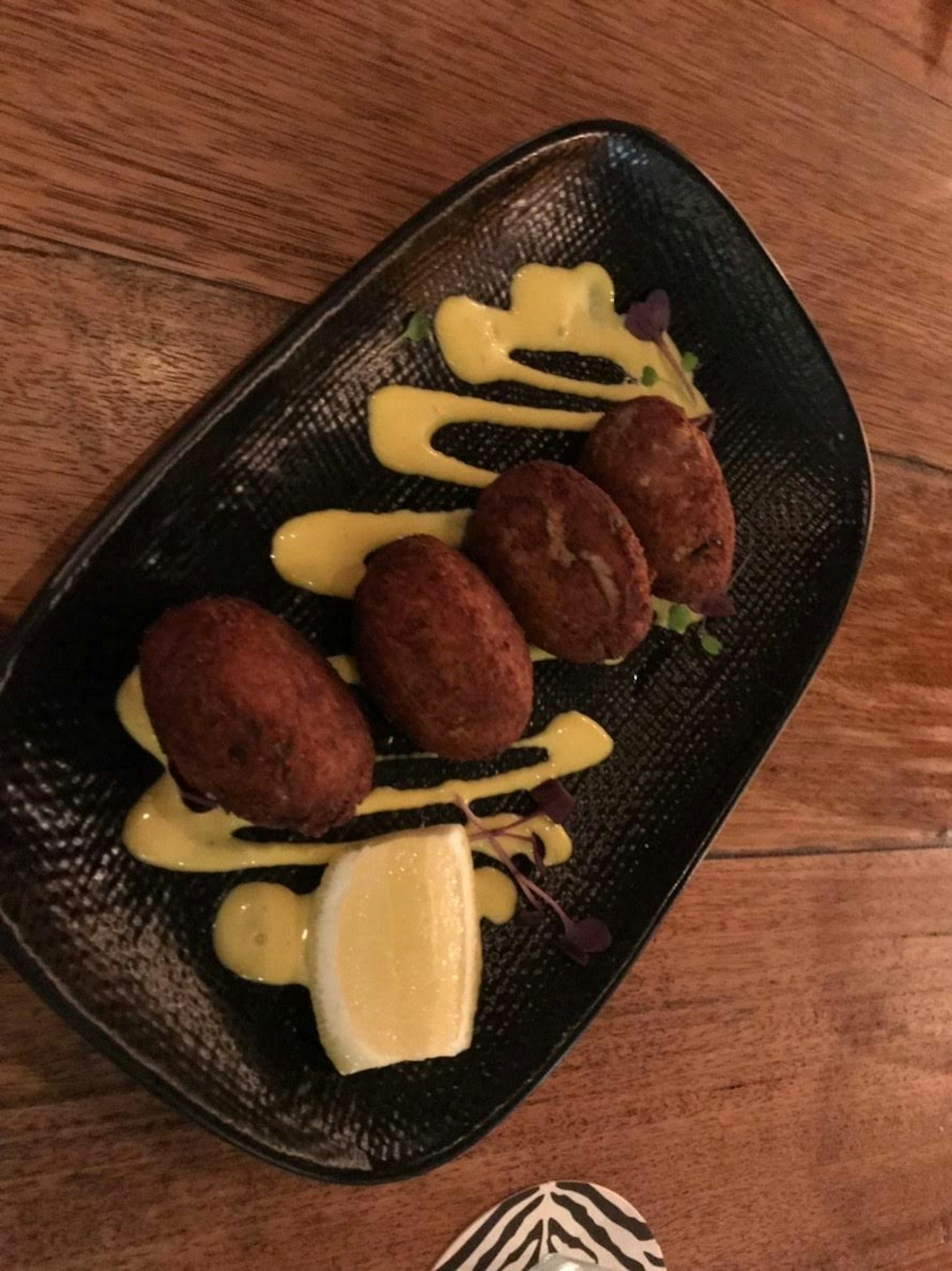 Vier Kroketten auf einem schwarzen Teller mit gelber Sauce