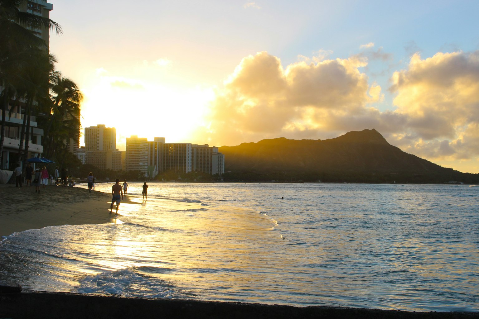 Personas en una playa hawaiana al atardecer con Diamond Head al fondo
