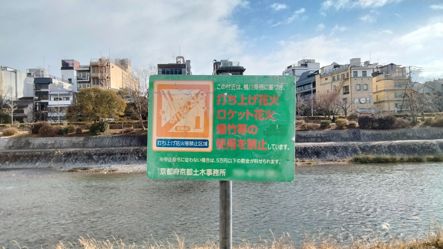 Panneau vert près de la rivière affichant une carte et des informations avec des bâtiments en arrière-plan