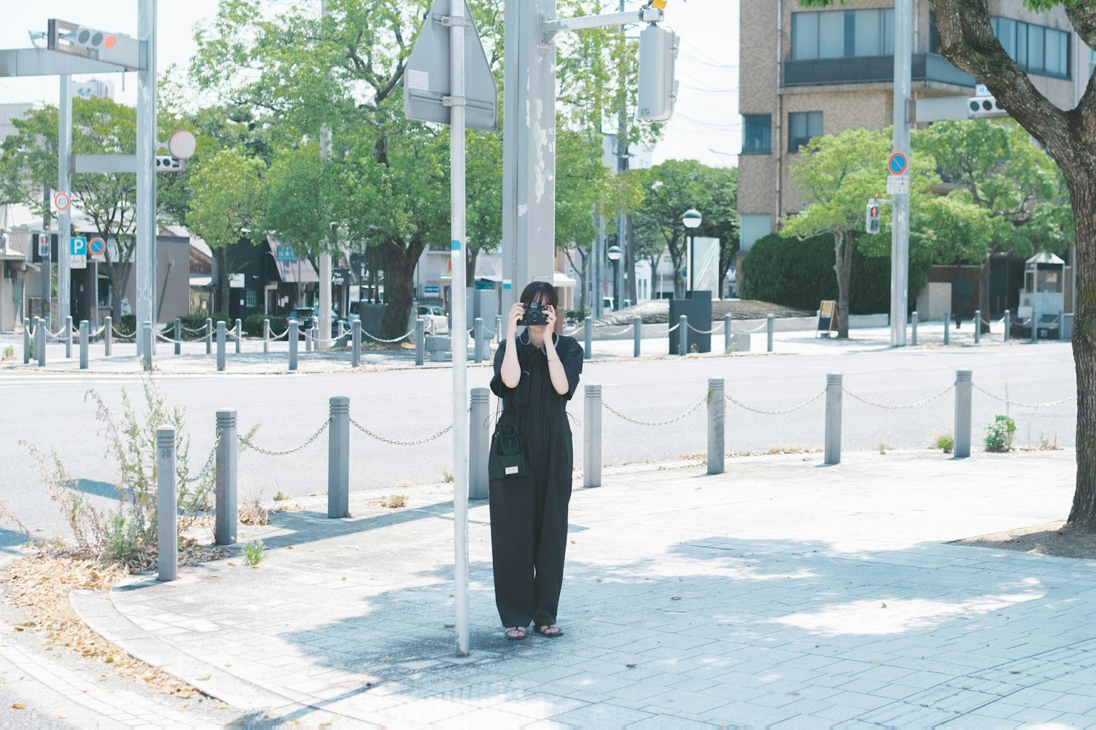 一位穿着黑色衣服的女性站在街角，手持相机