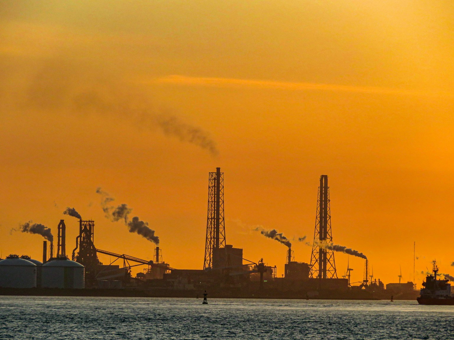 Silhouette eines Industriegebiets bei Sonnenuntergang mit Schornsteinen und Lagertanks