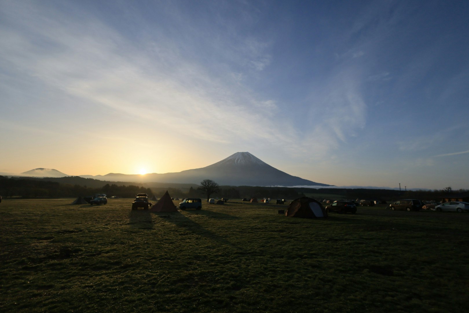 tents on a grassy field with a distant mountain at sunset