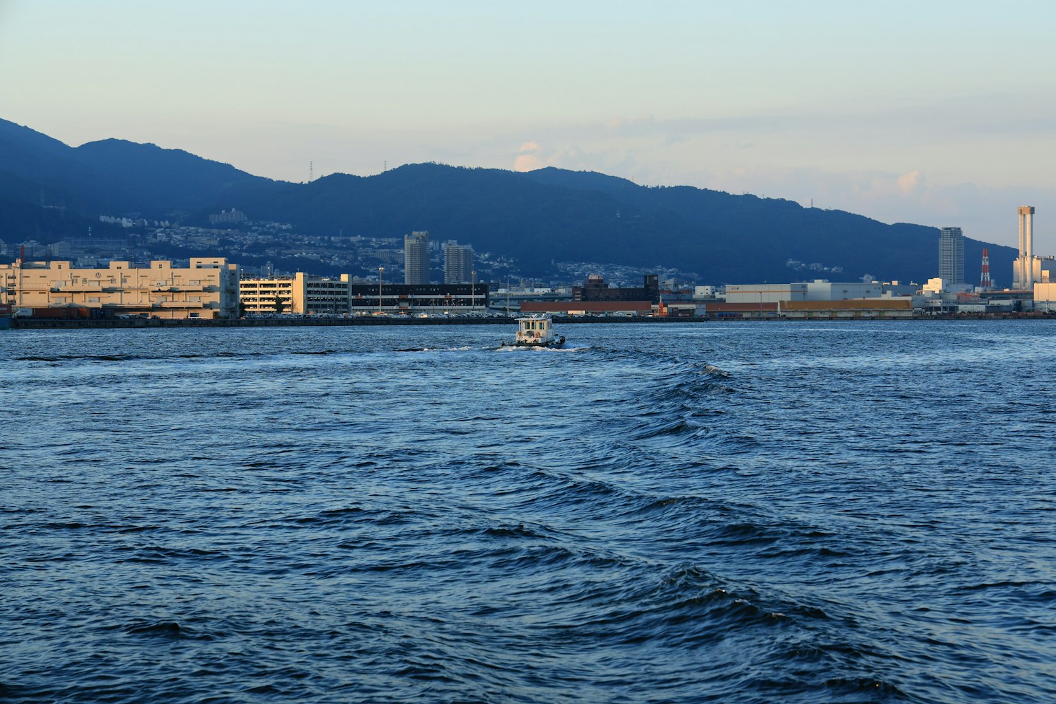 Ein kleines Boot, das auf blauem Wasser mit Bergen im Hintergrund fährt