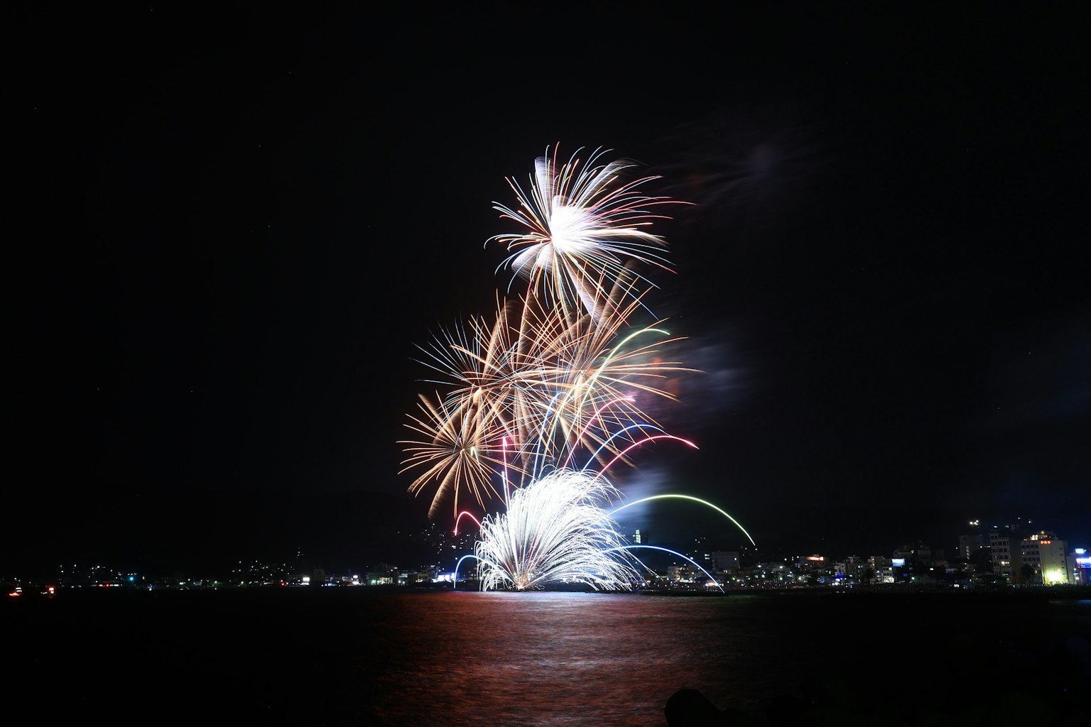 Fuochi d'artificio colorati illuminano il cielo notturno sopra l'acqua