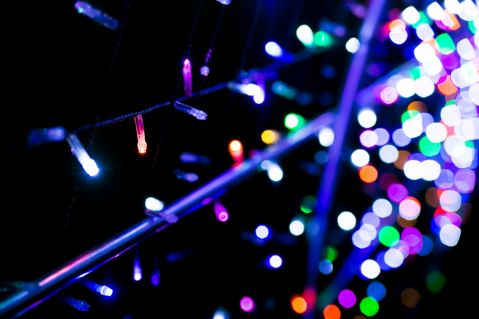 Colorful Christmas lights glowing against a dark background on thin wires