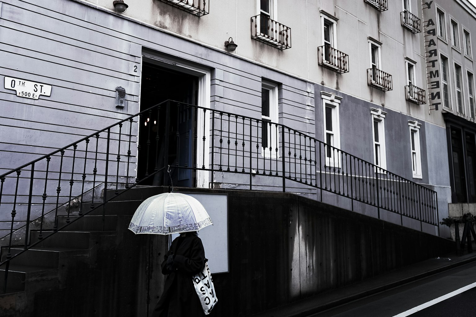 Una persona che cammina davanti a un edificio grigio con un ombrello bianco