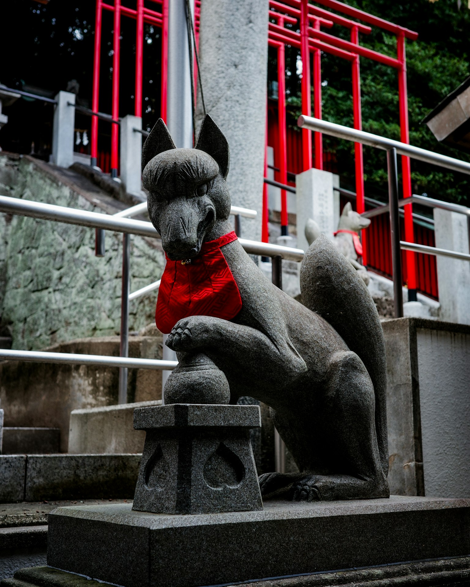 Steinstatue eines Fuchses mit rotem Schal an einer Treppe eines Schreins