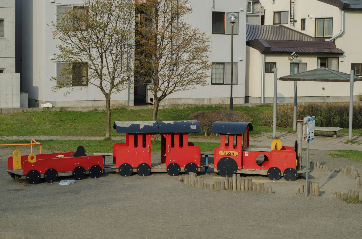 A set of red playground train and cargo car in a park