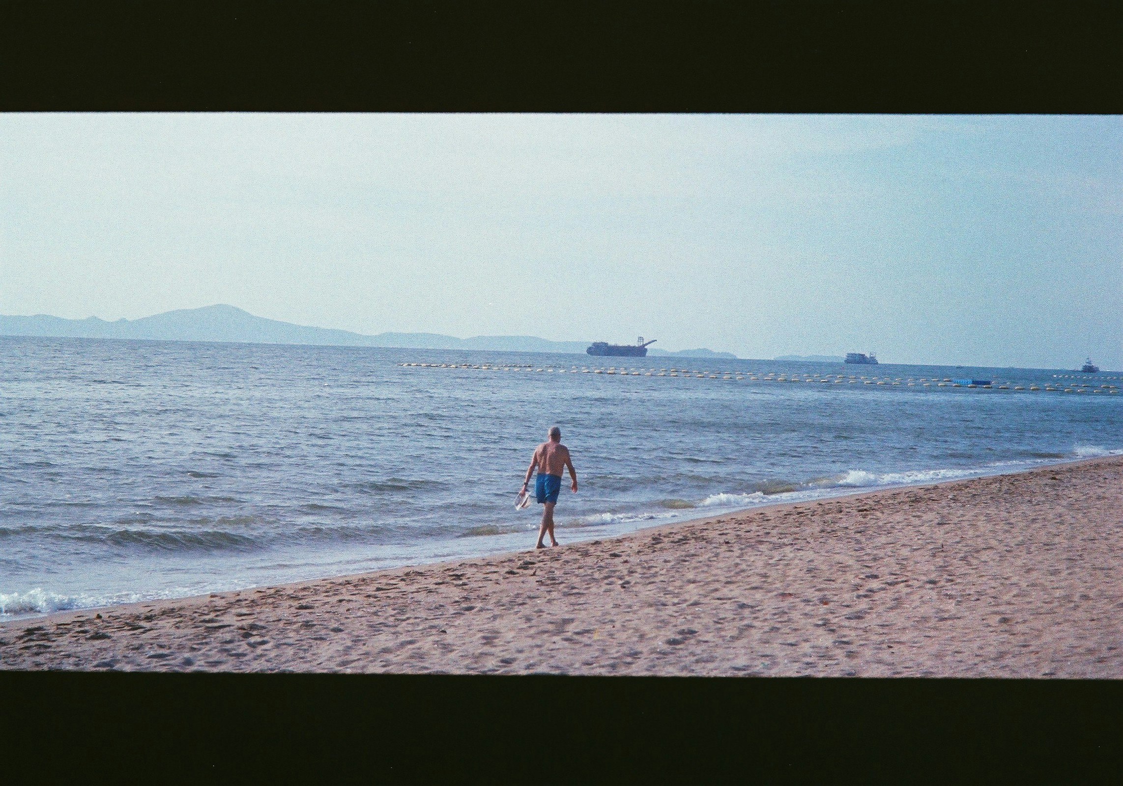 คนเดินบนชายหาดทรายพร้อมเรือที่อยู่ไกลๆ