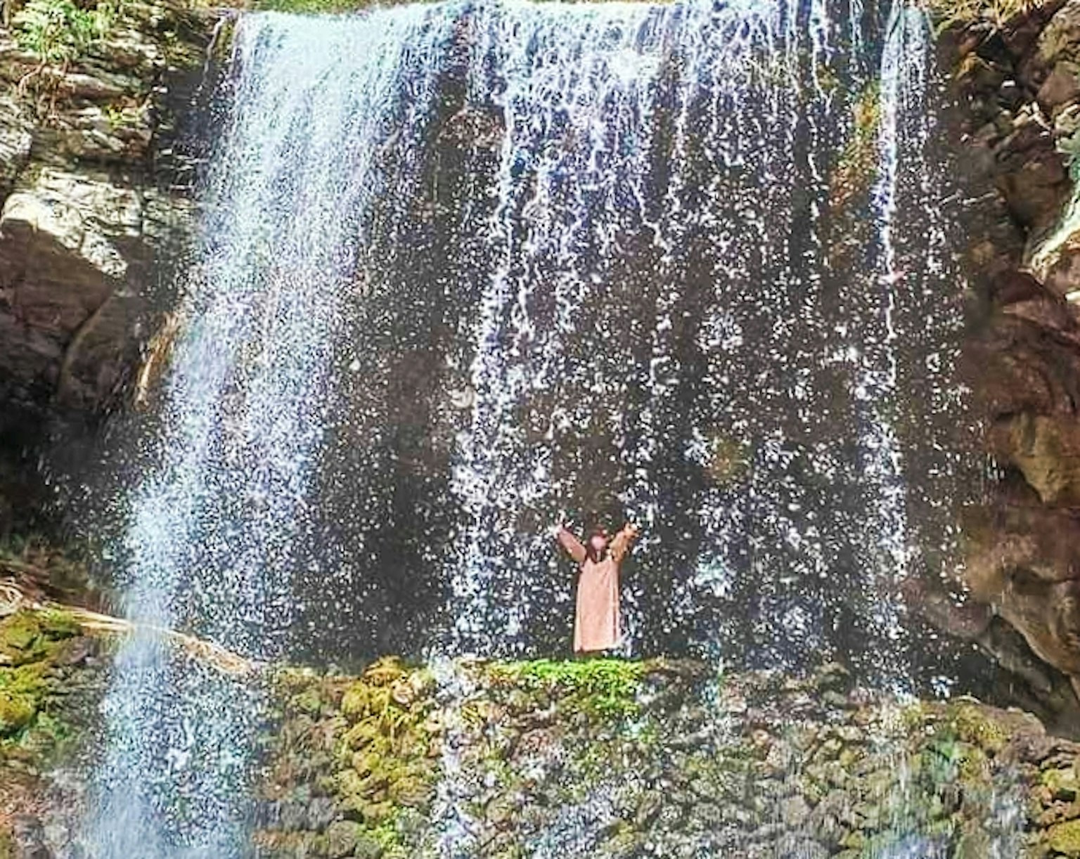 Orang yang berdiri di depan air terjun dengan percikan air yang indah