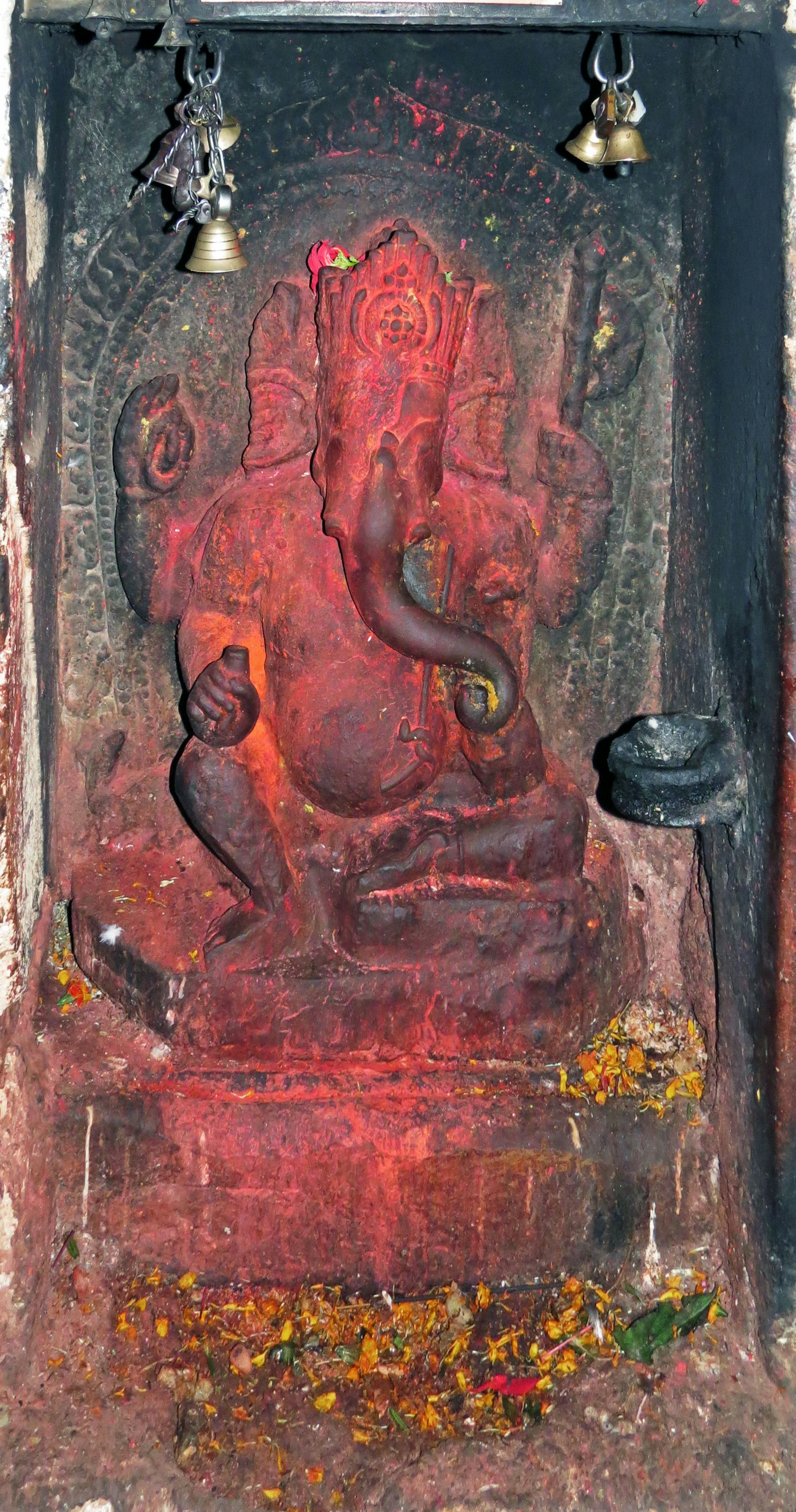 Statua di Ganesh rossa su un altare circondata da petali di fiori e un porta-incenso