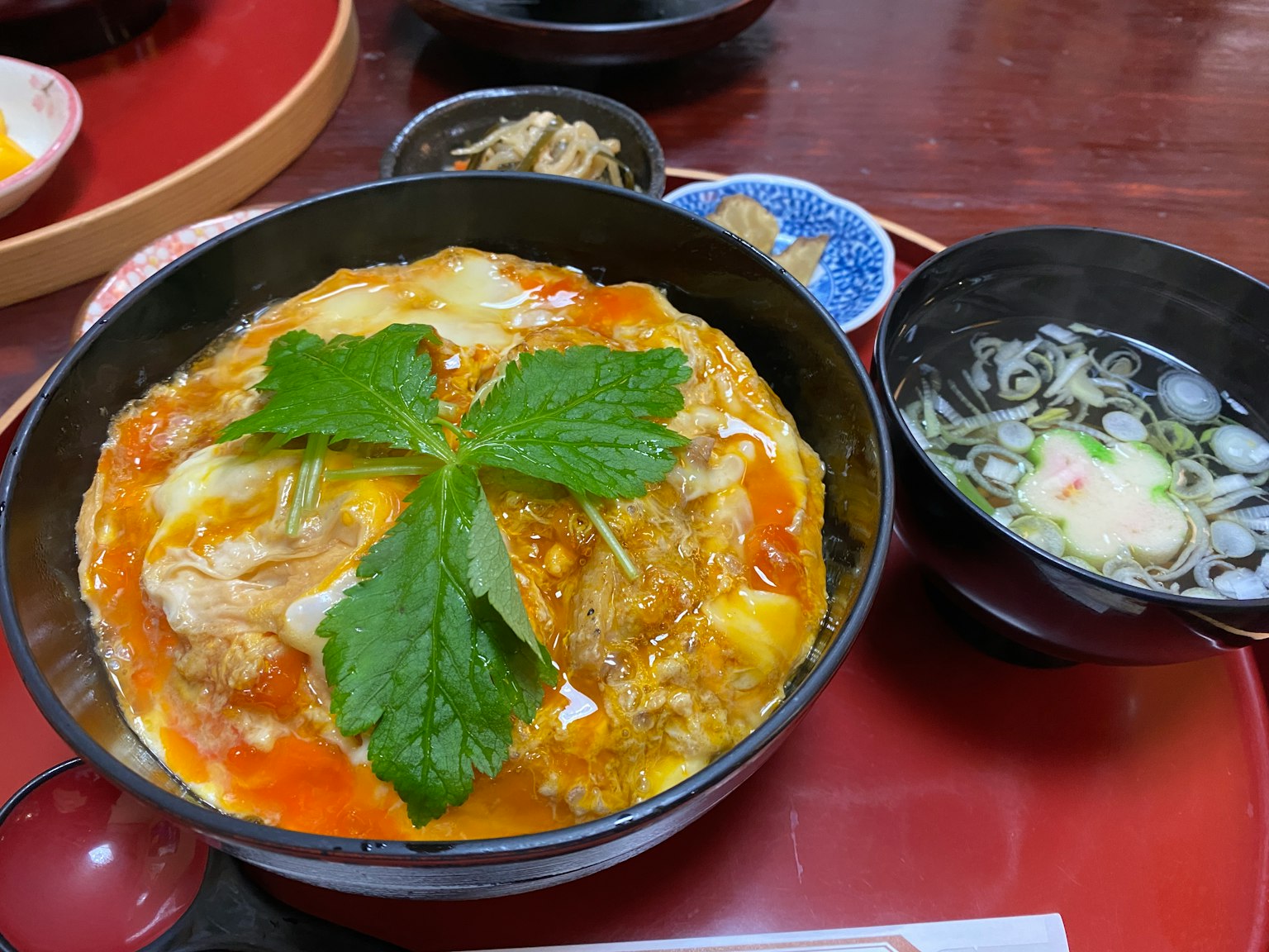 A bowl of oyakodon topped with green leaves alongside a bowl of miso soup