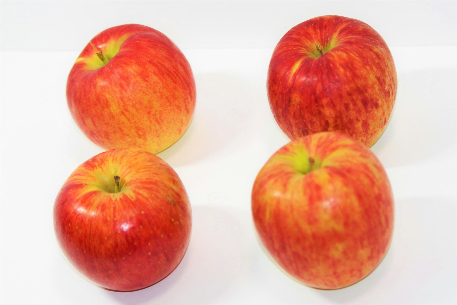 Cuatro manzanas rojas dispuestas sobre un fondo blanco