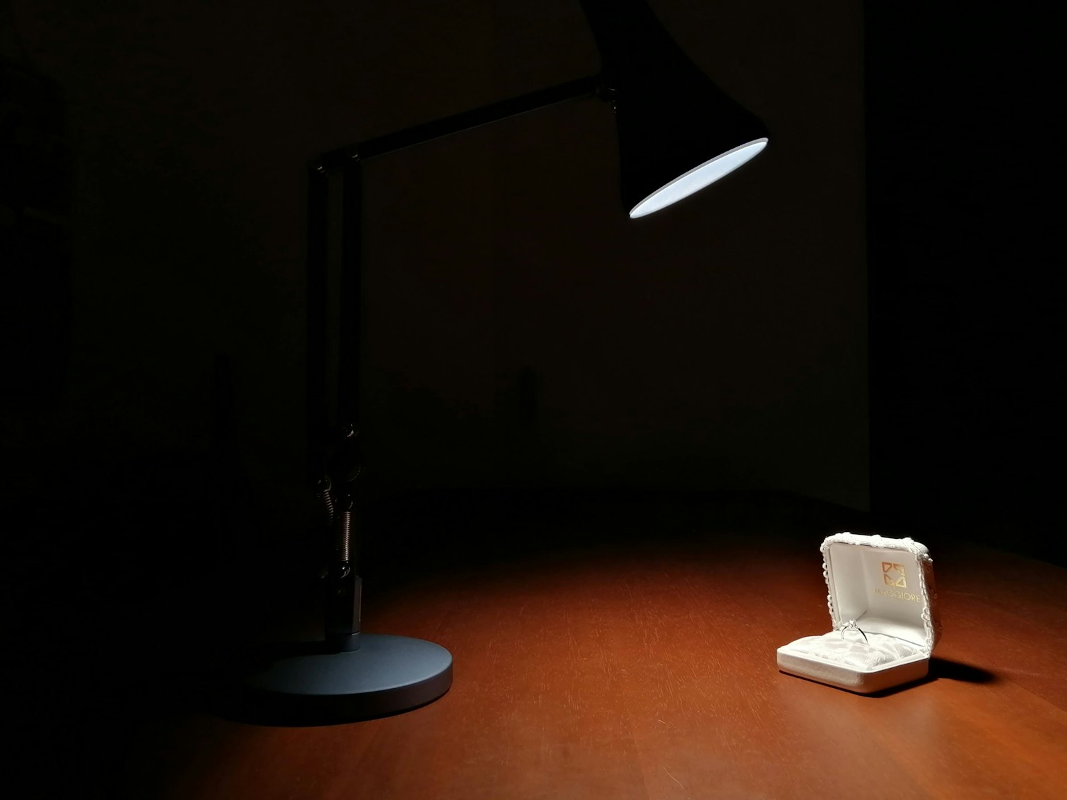 Black desk lamp illuminating a white jewelry box on a wooden table