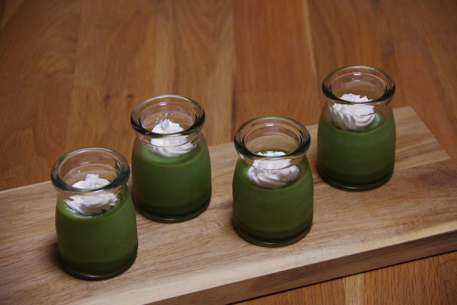Vier kleine Glasbehälter mit grünem Dessert und Sahnehaube