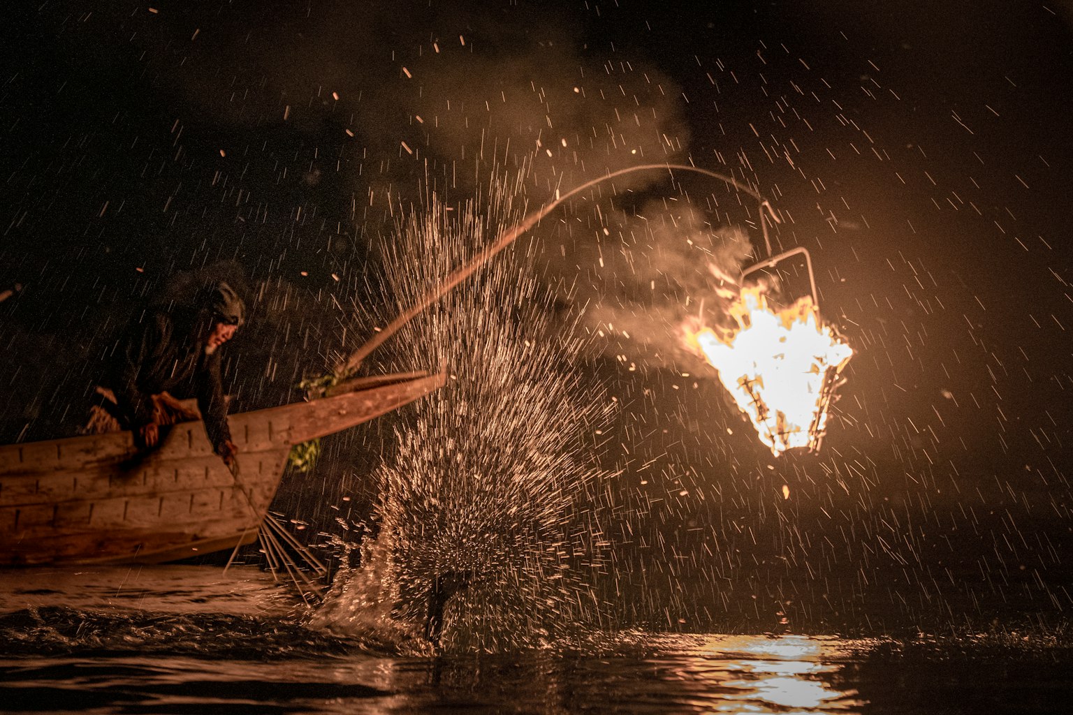 Pescatore in una piccola barca di notte che lancia un oggetto infuocato nell'acqua