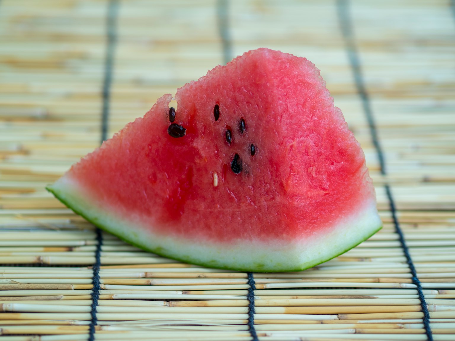 Una fetta di anguria appoggiata su un tappetino di bambù