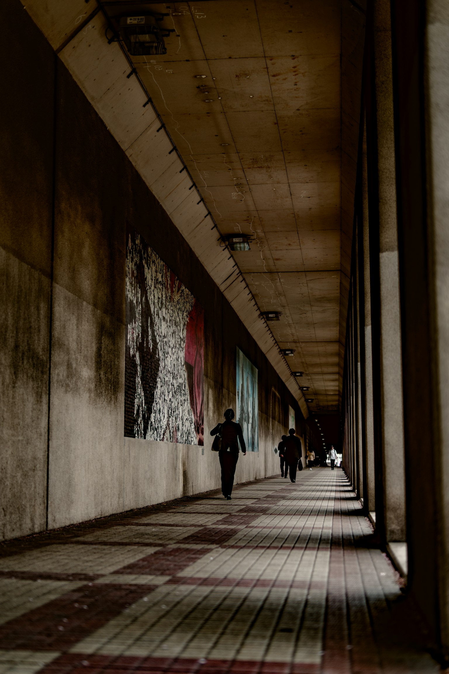 Largo corredor de concreto con obras de arte y figuras sombreadas