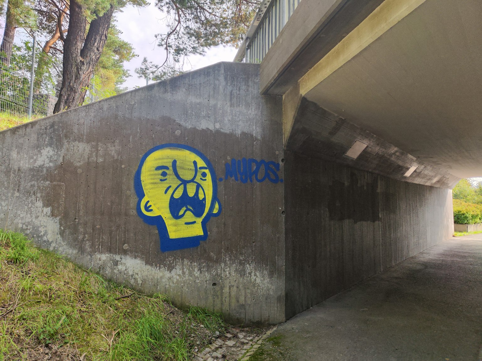 Graffiti giallo vivace di un volto espressivo sotto un ponte
