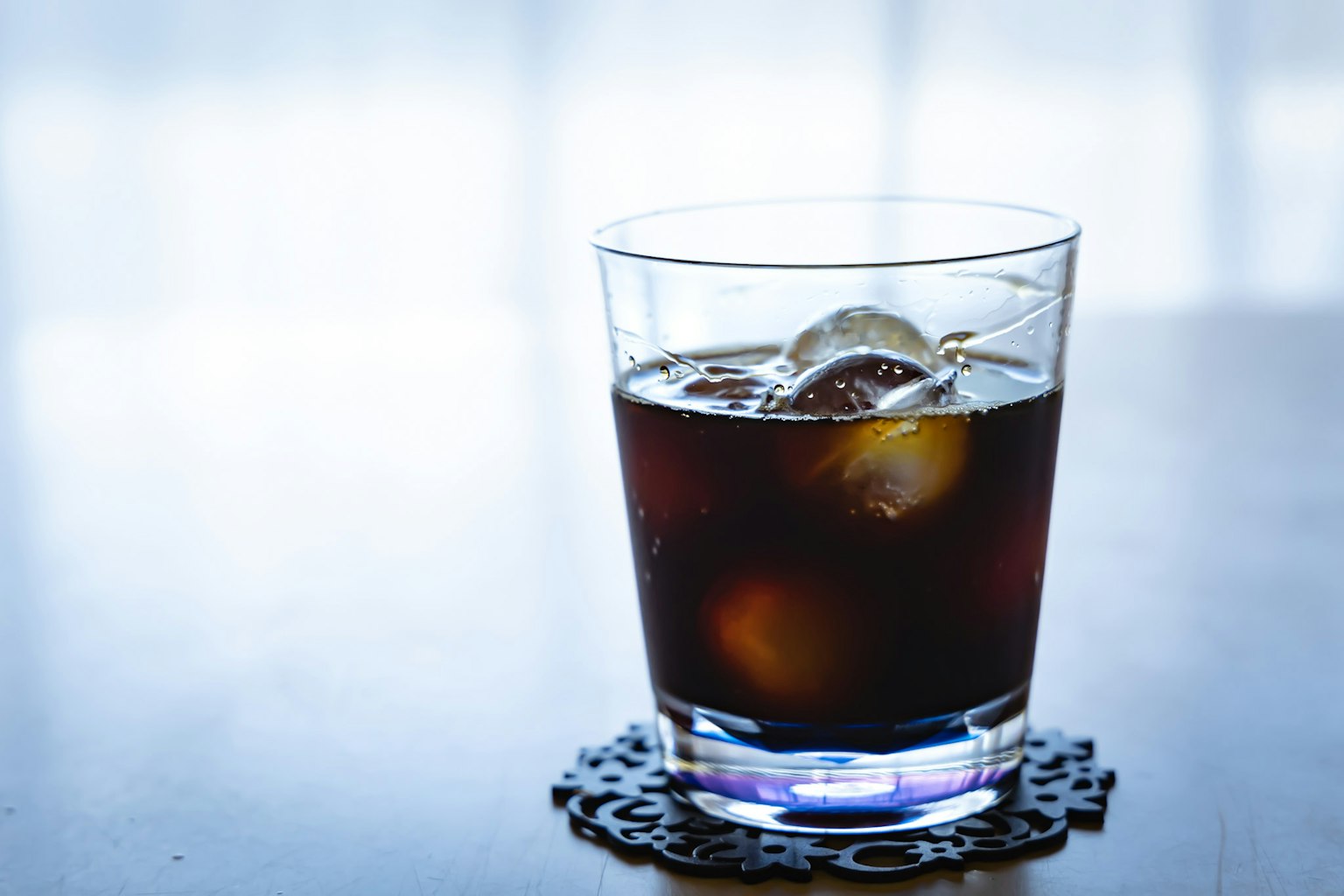 Gelas minuman gelap dengan es batu di atas tatakan dekoratif
