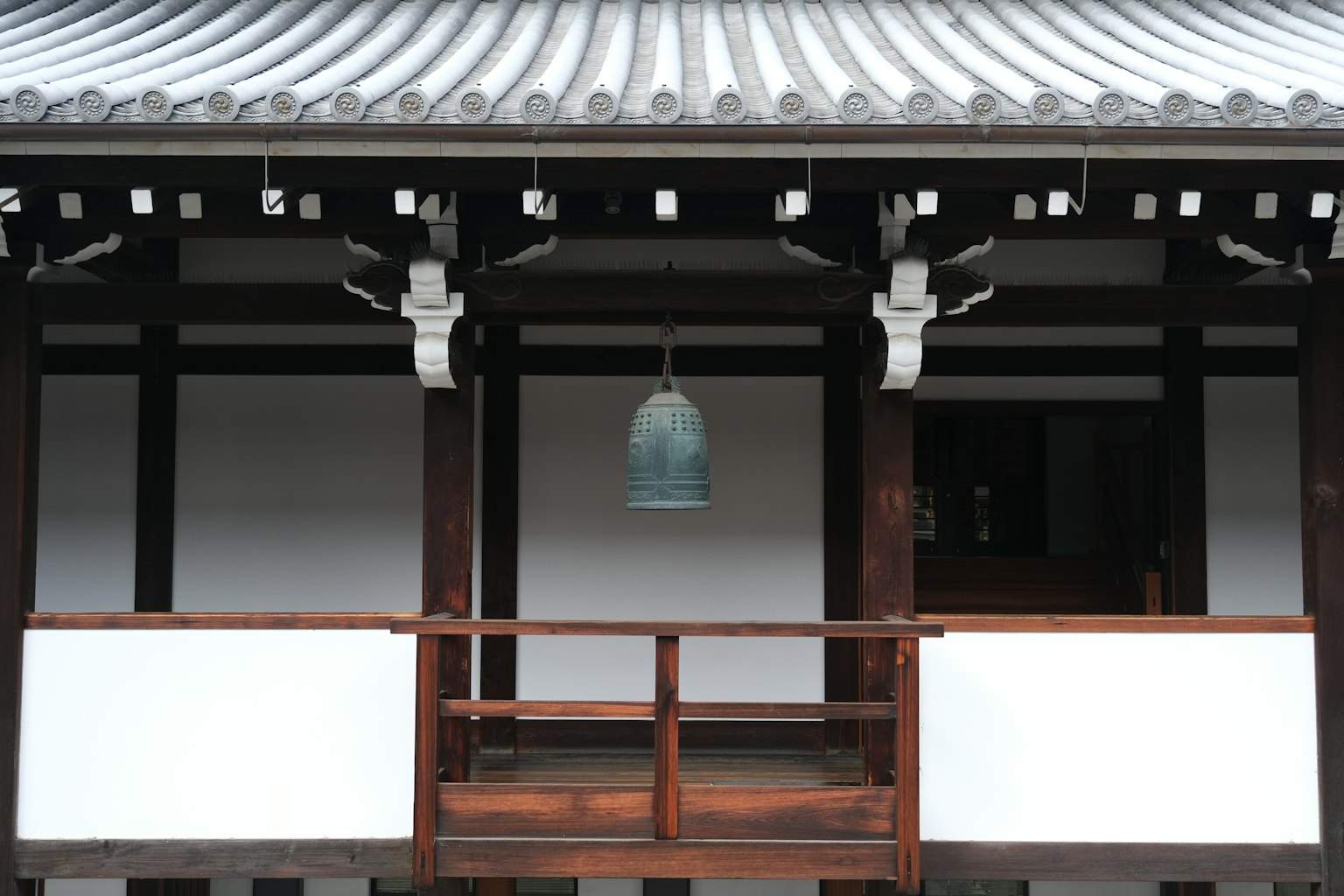 傳統日本建築外觀，木製陽台上懸掛著一口鐘，白色牆壁