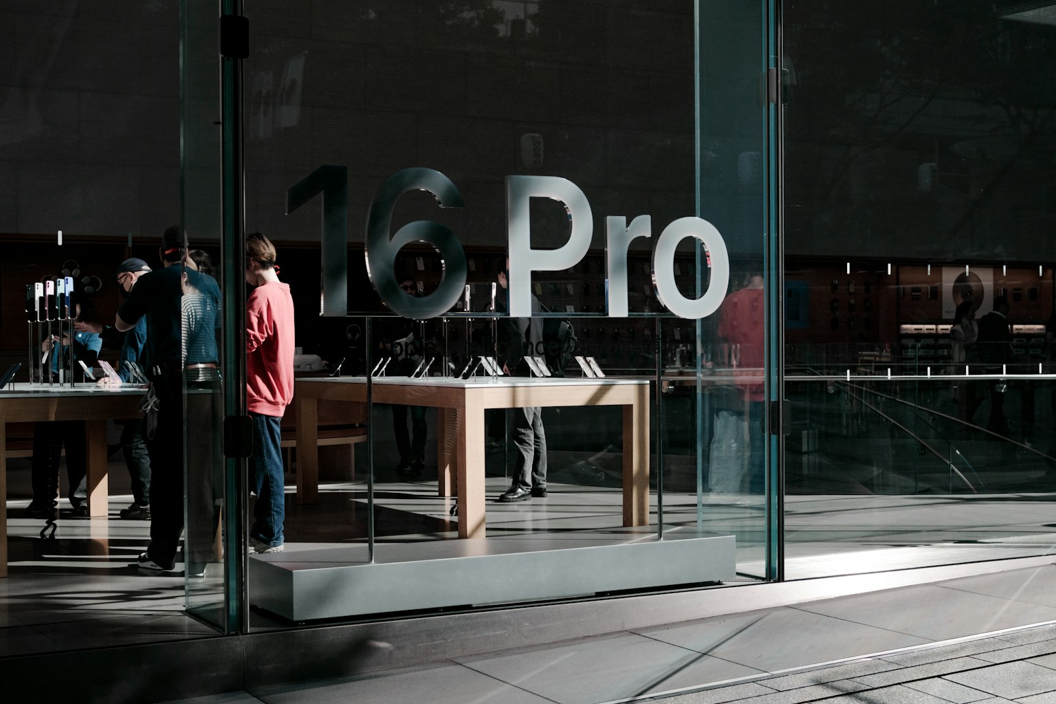 Cửa vào của Apple Store có '16 Pro' trên kính và khách hàng đang xem sản phẩm