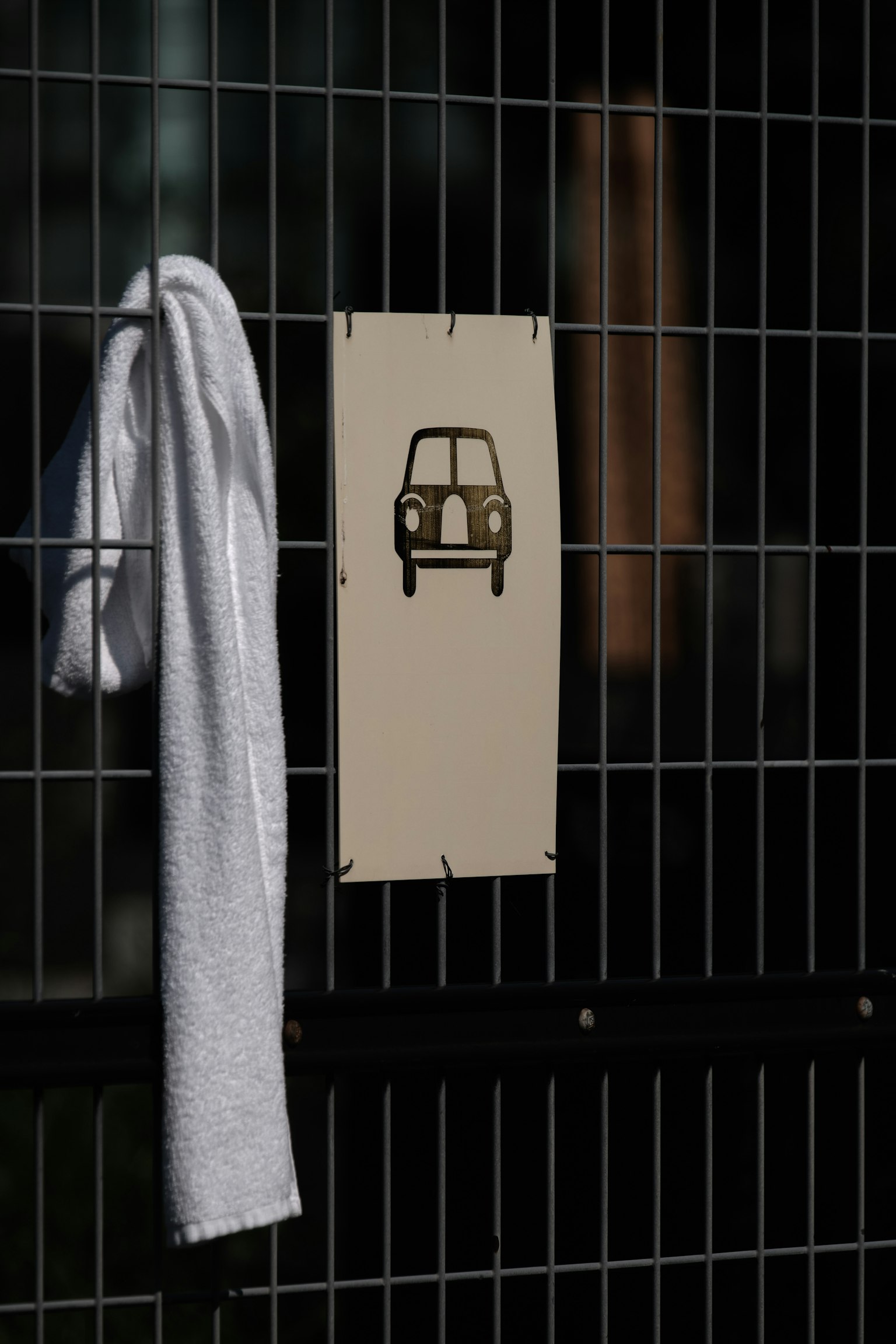 Un asciugamano bianco appeso a una recinzione con un cartello che raffigura un'auto sullo sfondo