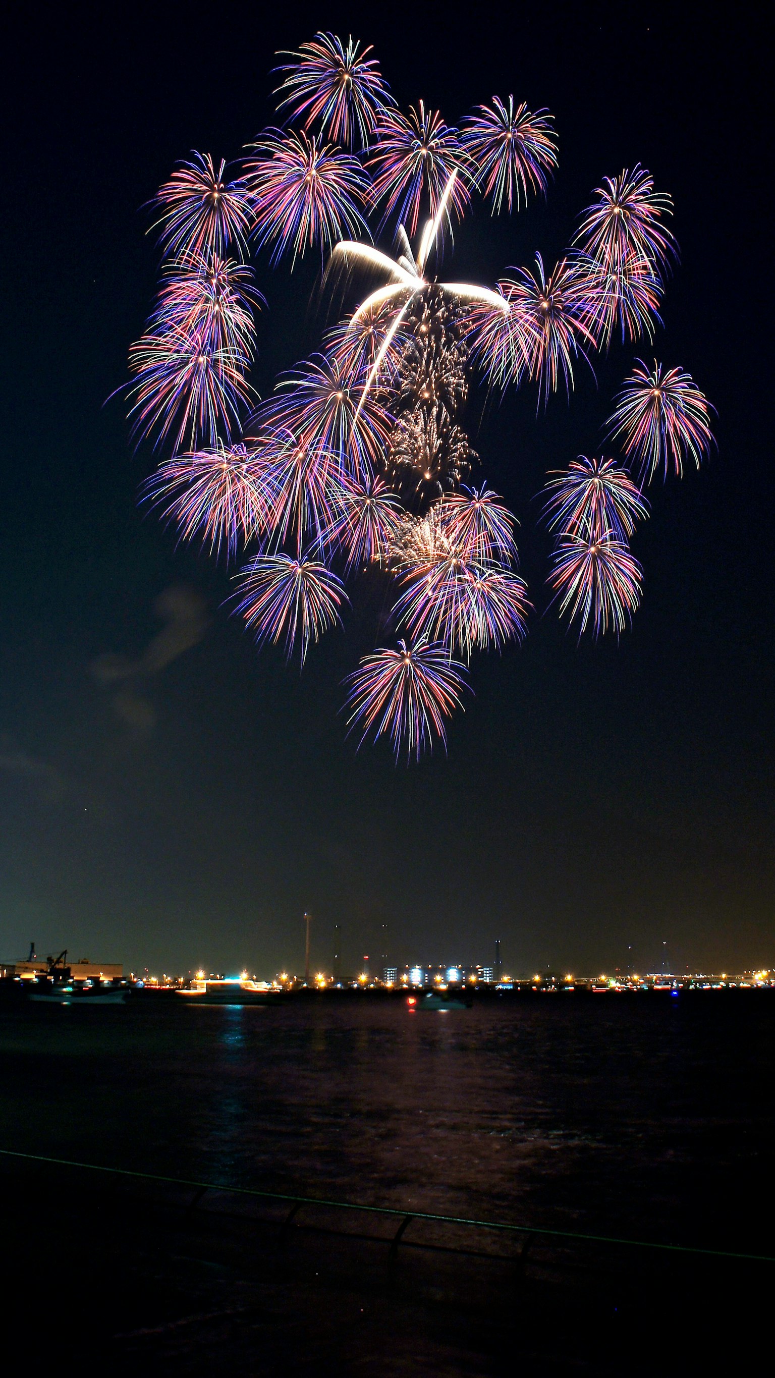 夜空に花火が咲いている光景で色とりどりの火花が水面に映る