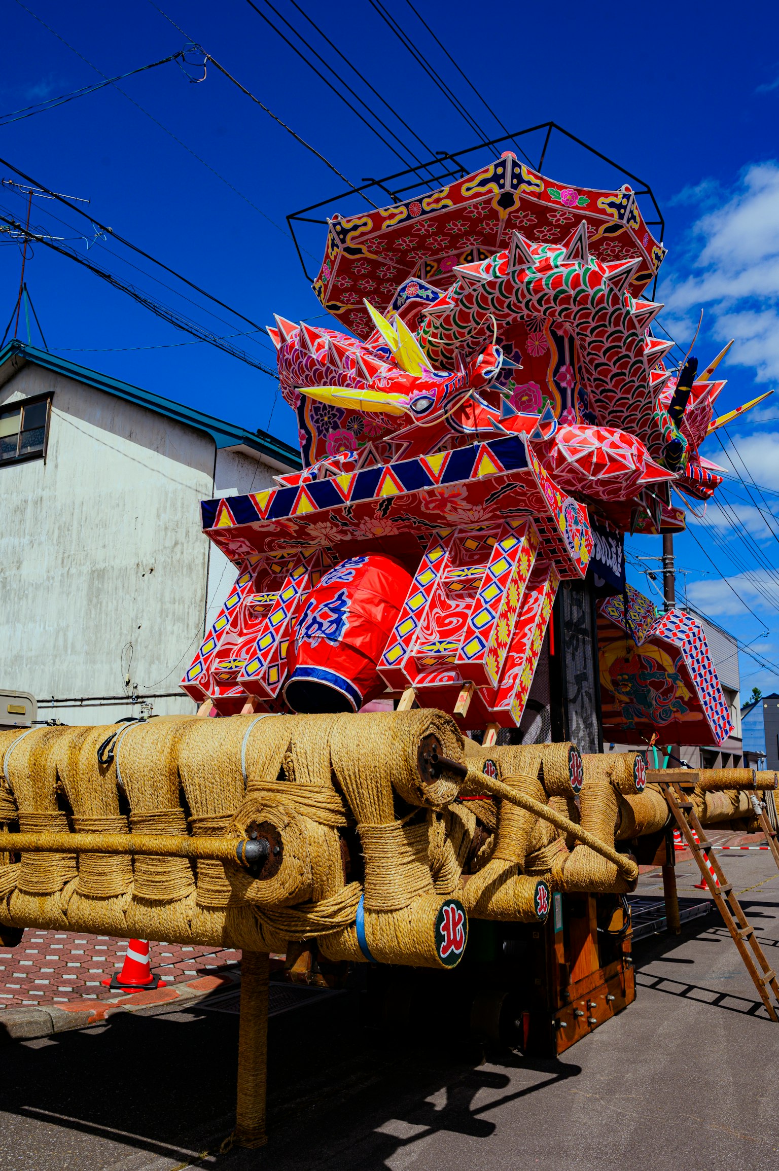 色とりどりの装飾が施された祭りの山車が青空の下に立っている