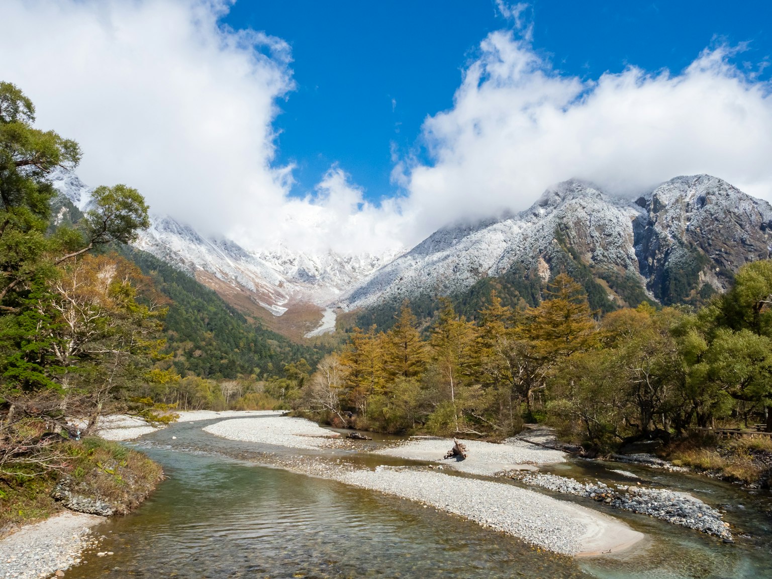 Malersicher Blick auf einen Fluss, der durch ein Tal mit schneebedeckten Bergen und blauem Himmel fließt