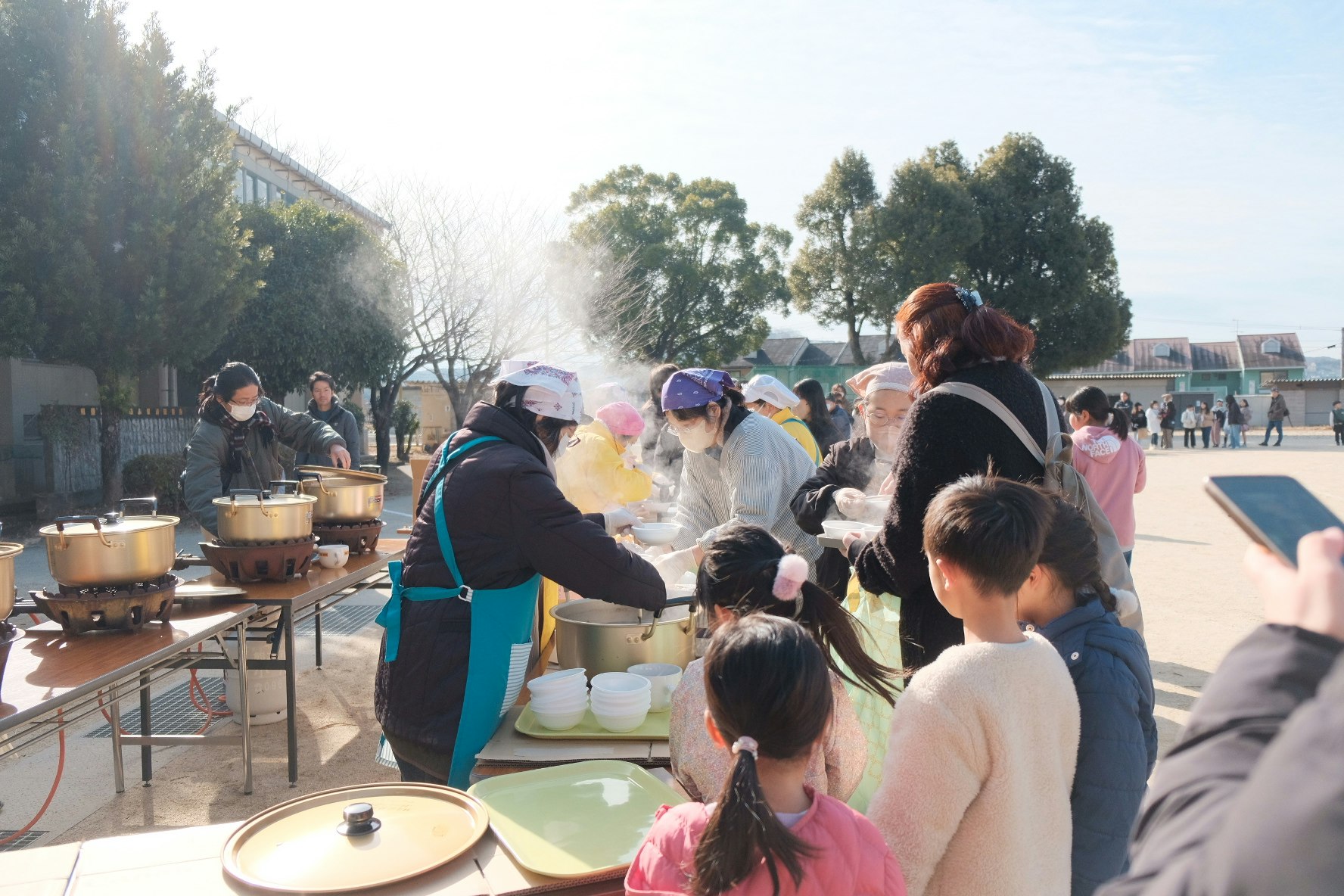 どんどやのぜんざい配布で湯気の立つ鍋を囲む人々