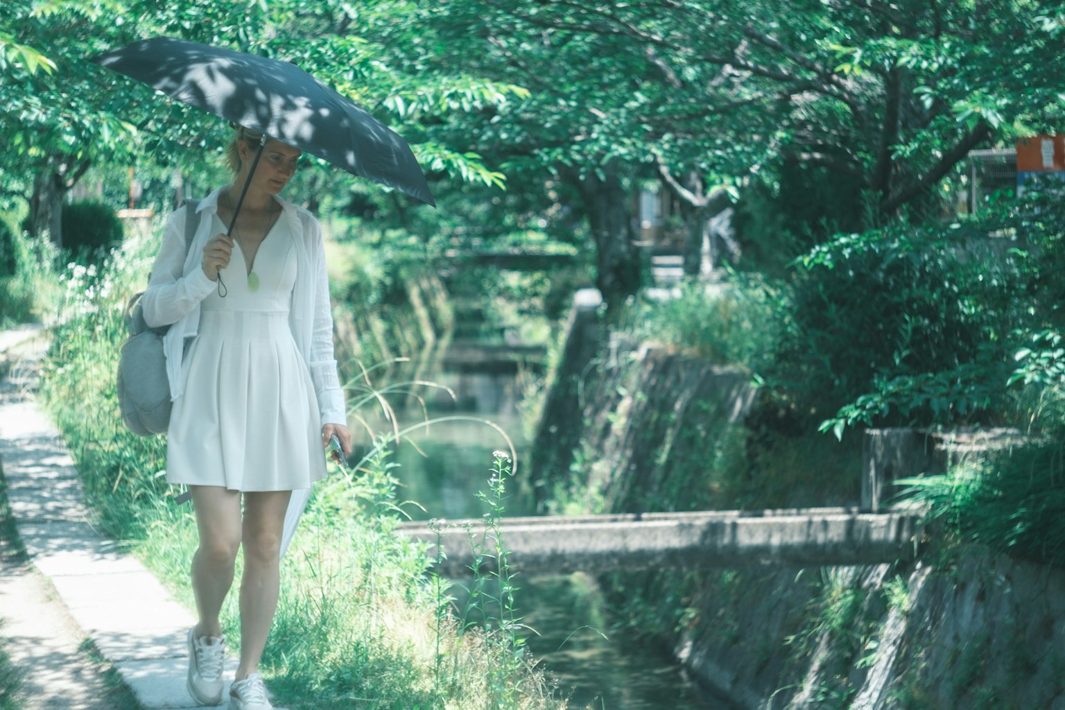 Donna in abito bianco che cammina con un ombrello in un ambiente verdeggiante