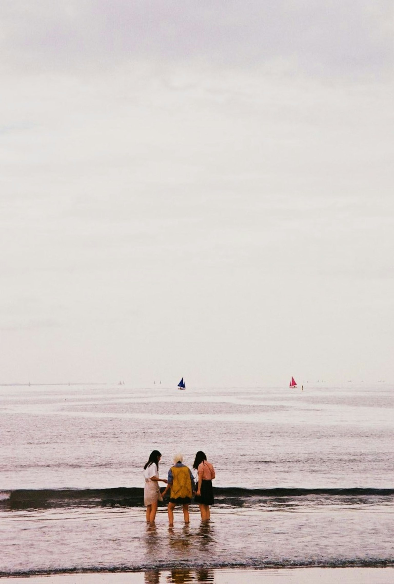 海辺で立つ三人の人々と遠くの帆船