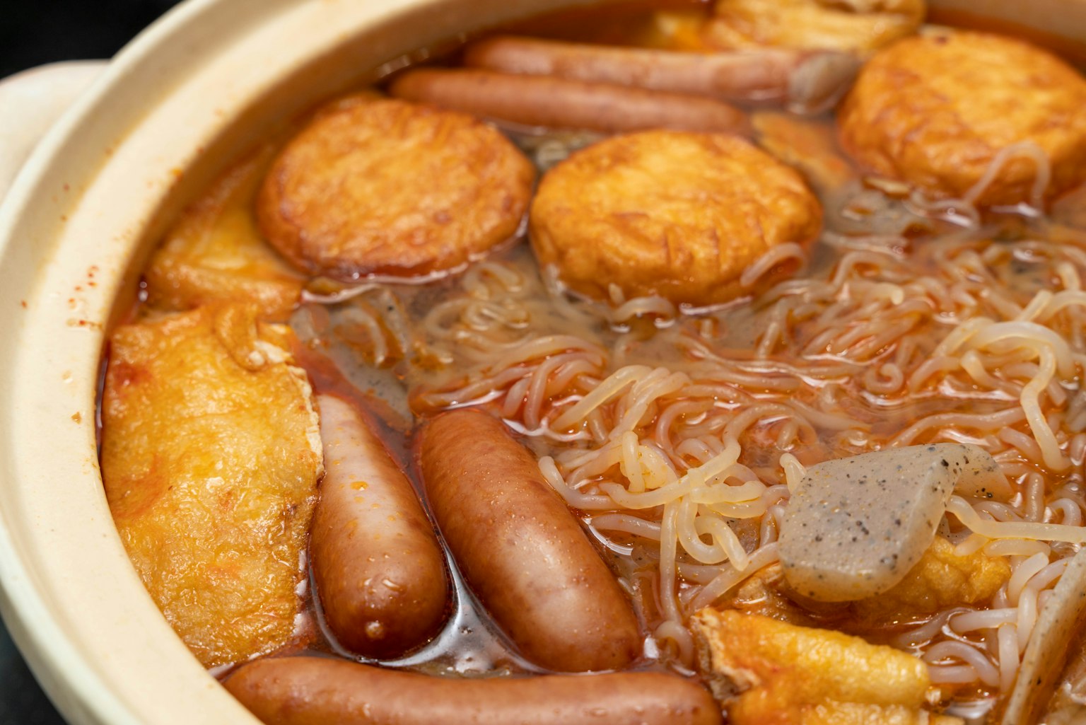 Nồi đầy xúc xích, bánh cá, mì và nước dùng