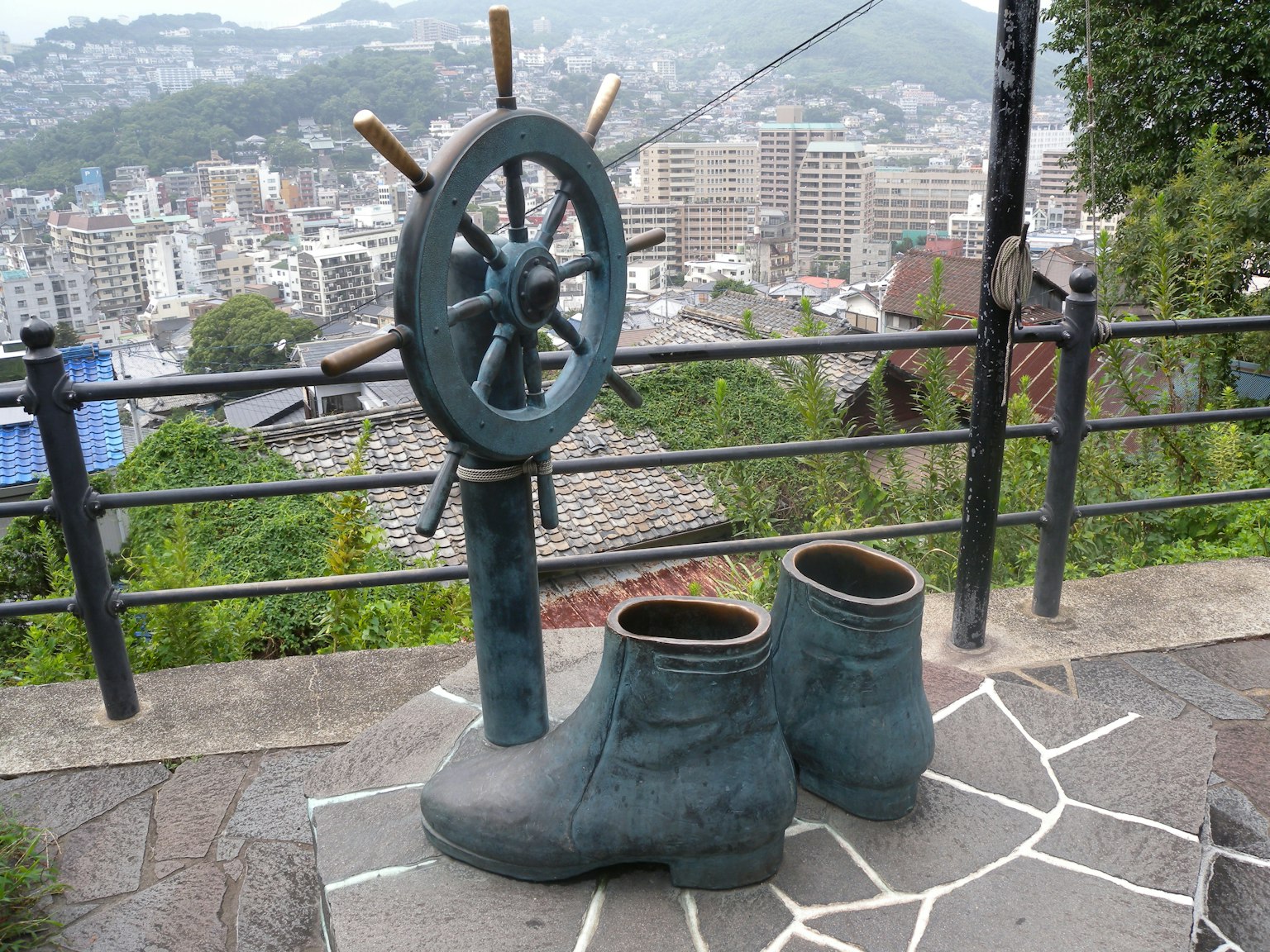 Escultura que presenta un timón y botas con vista a la ciudad