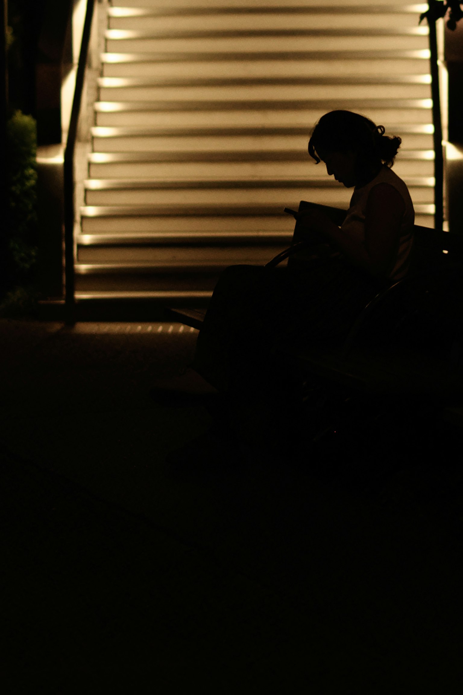 Silhouette of a person sitting in a dark setting with bright stairs in the background