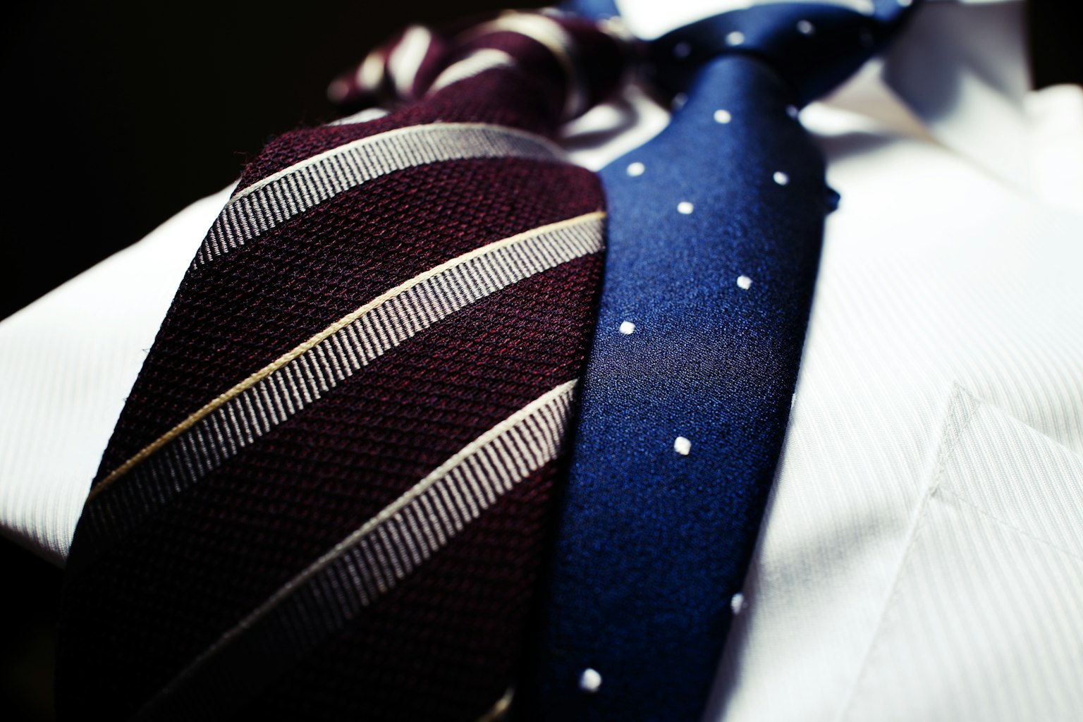 Primer plano de una camisa blanca con una corbata burdeos a rayas y una corbata azul con lunares