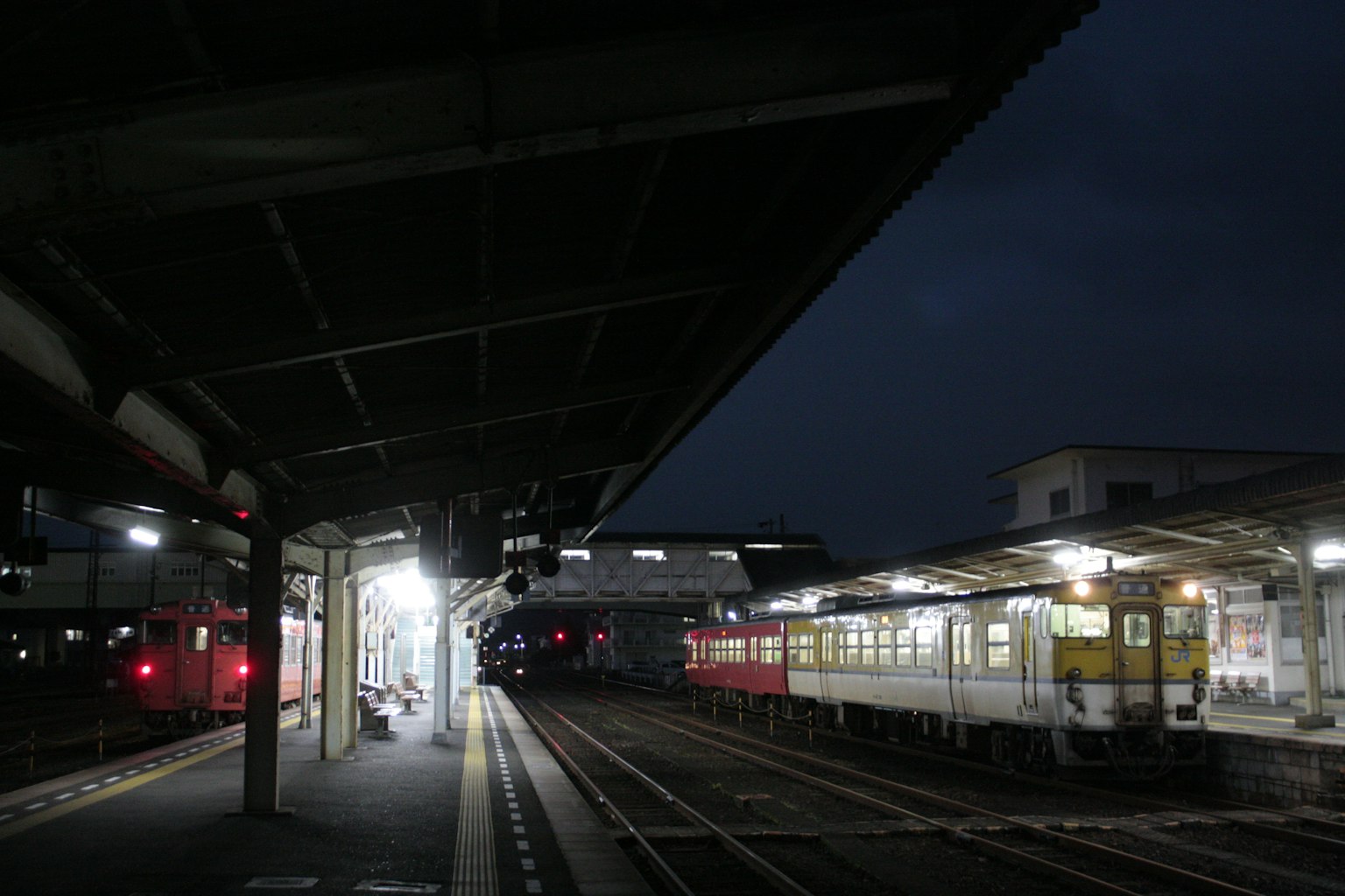 Stazione ferroviaria di notte con piattaforma illuminata e treni parcheggiati