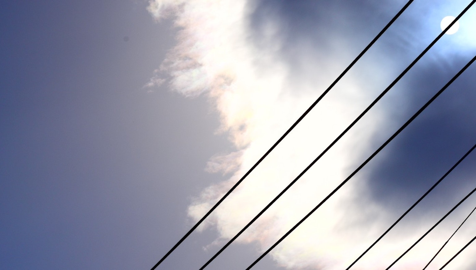 Foto di linee elettriche contro un cielo blu con nuvole bianche
